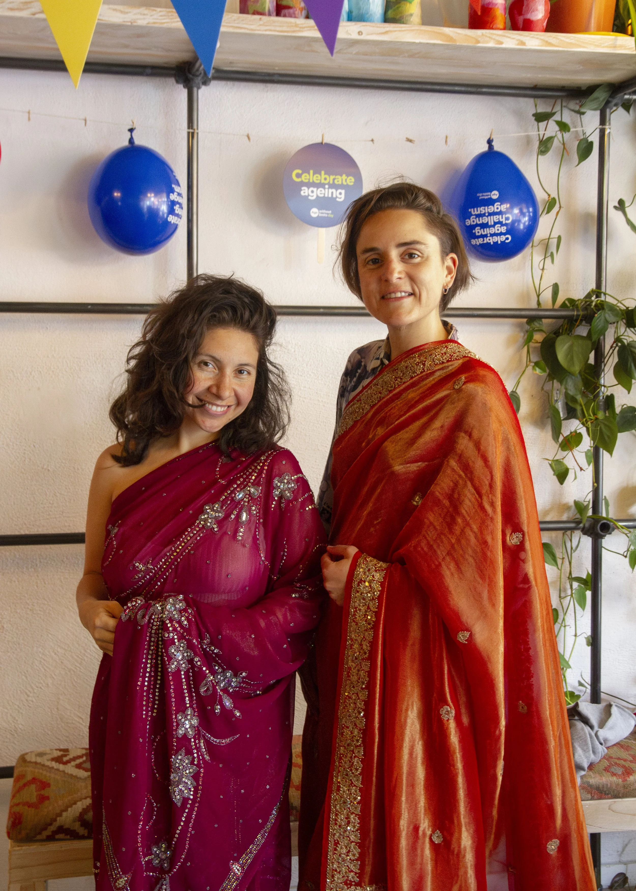 Two European women dressed in sarees stand straight and smile at the camera