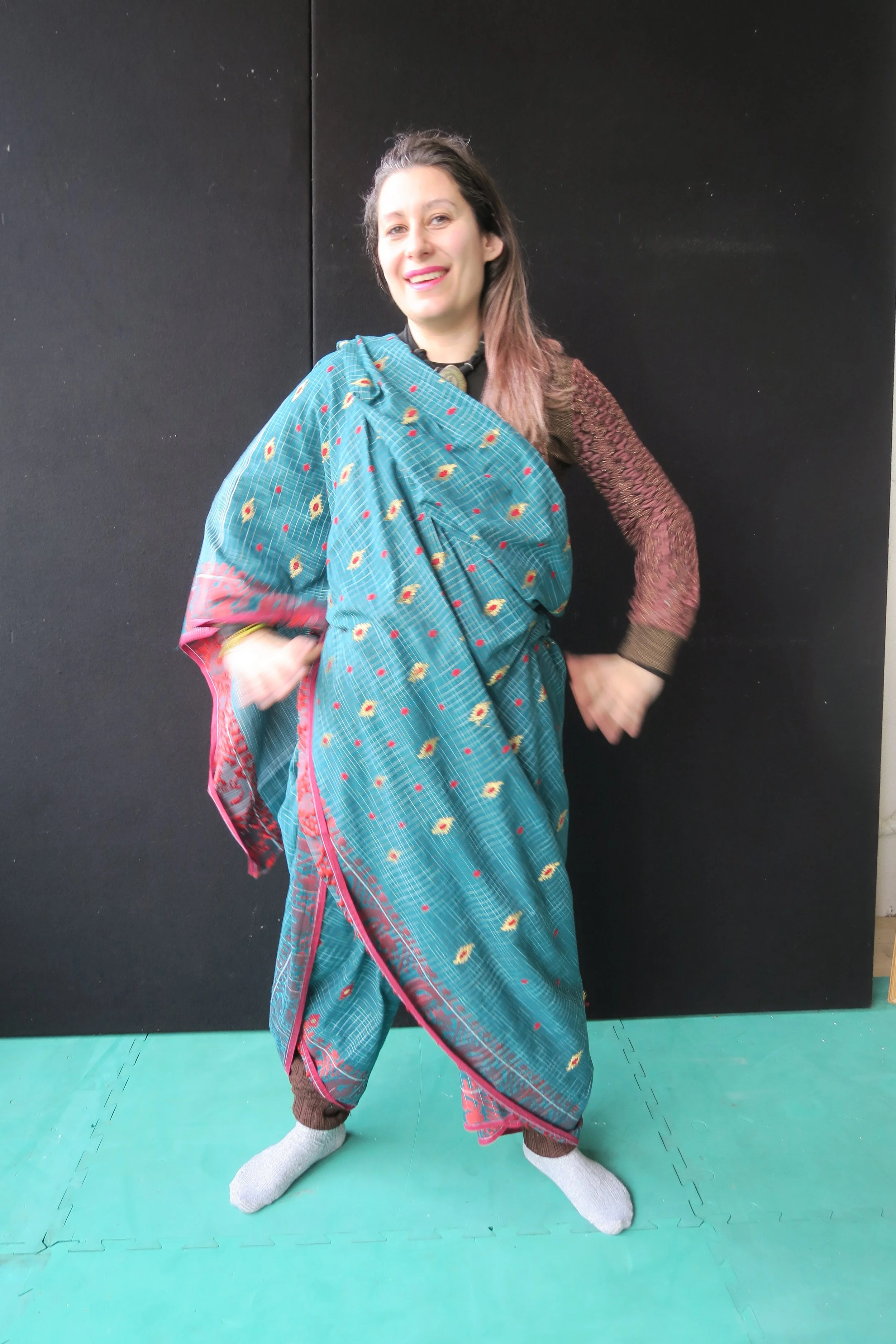 A white British woman wearing a green saree in a trouser drape with hands on her hips