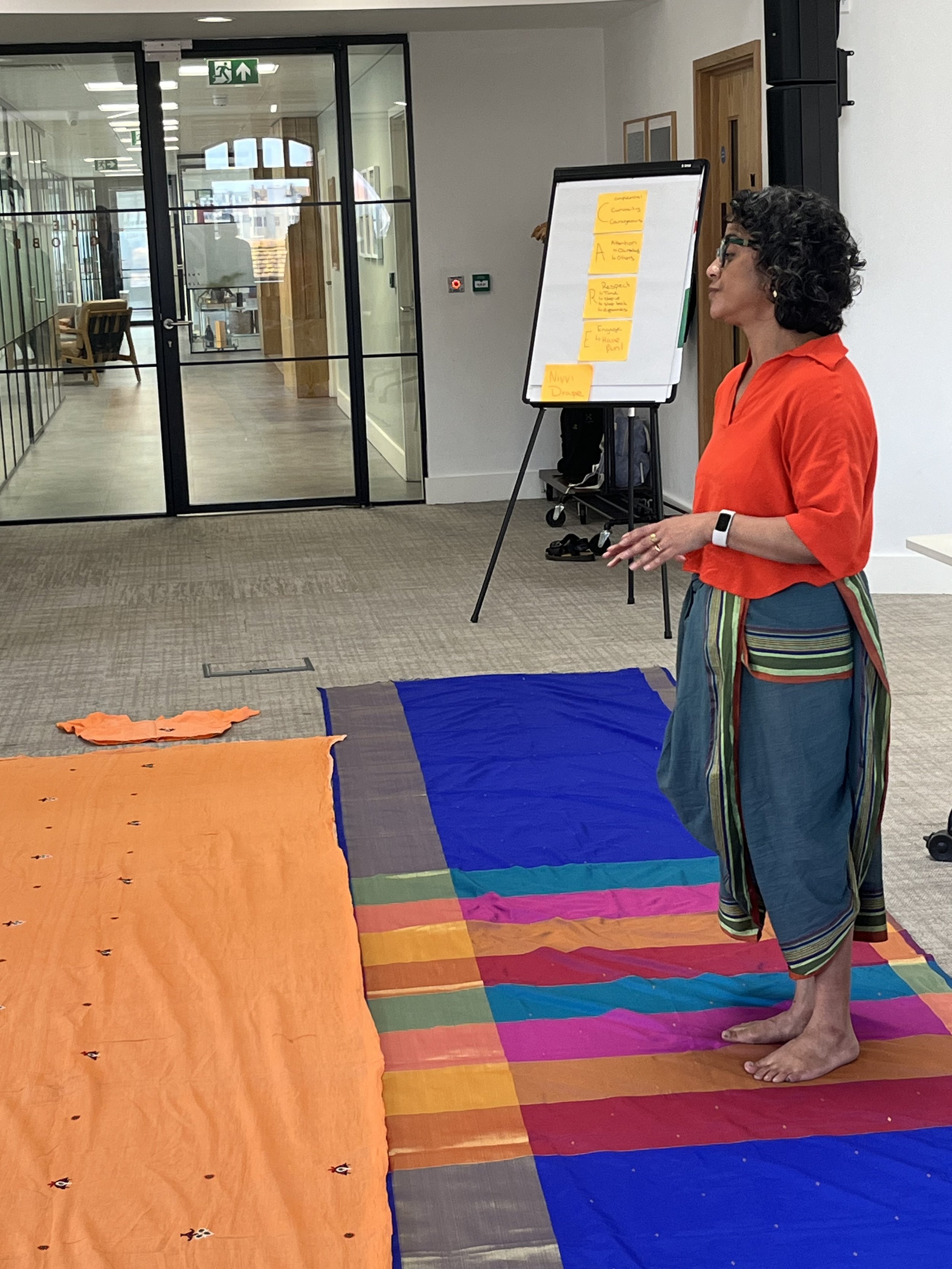 Poppy stands at the front of a room, on top of a colourful stripy saree