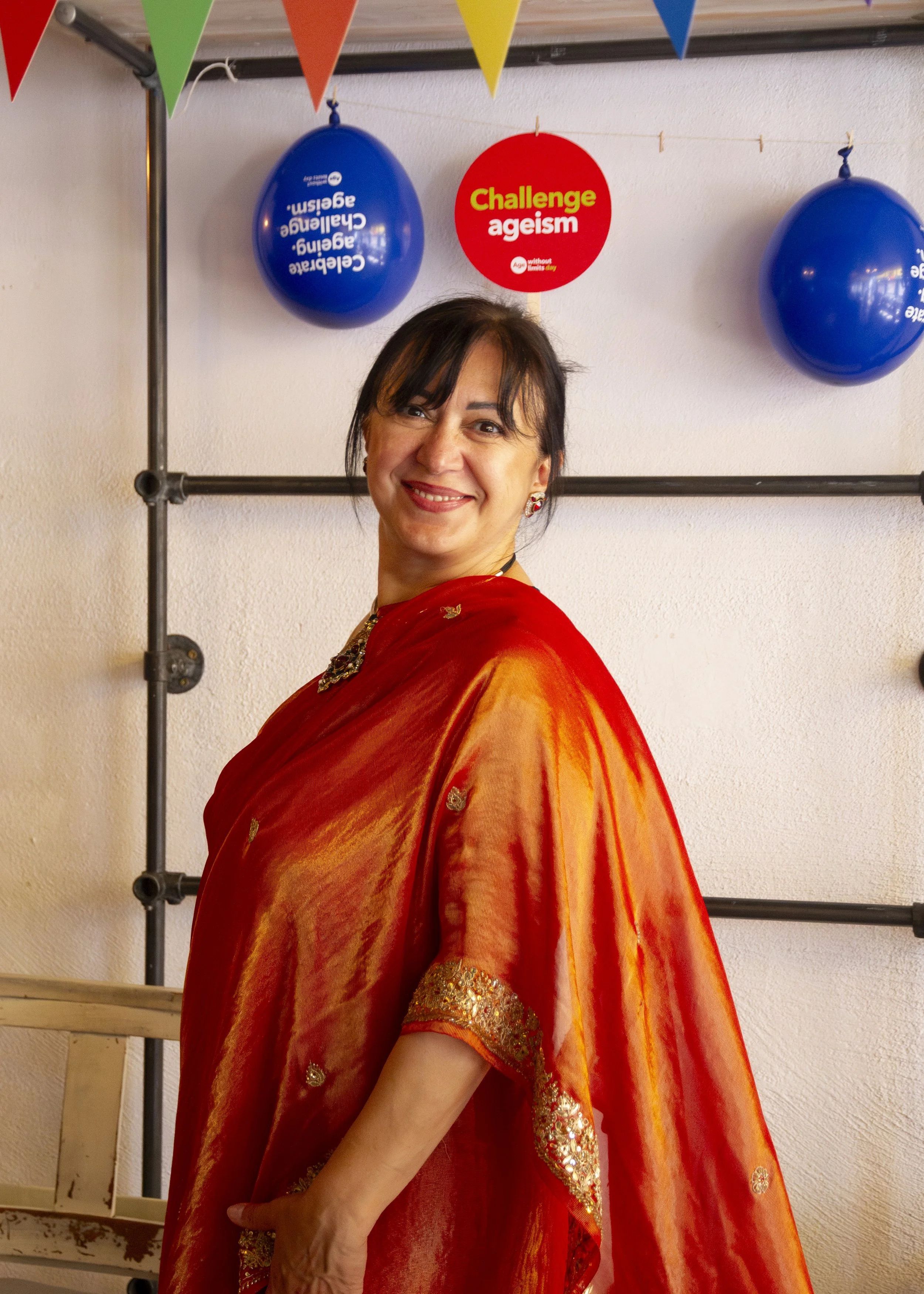 A Ukranian woman wearing an orange saree stands on her side and smiles at the camera