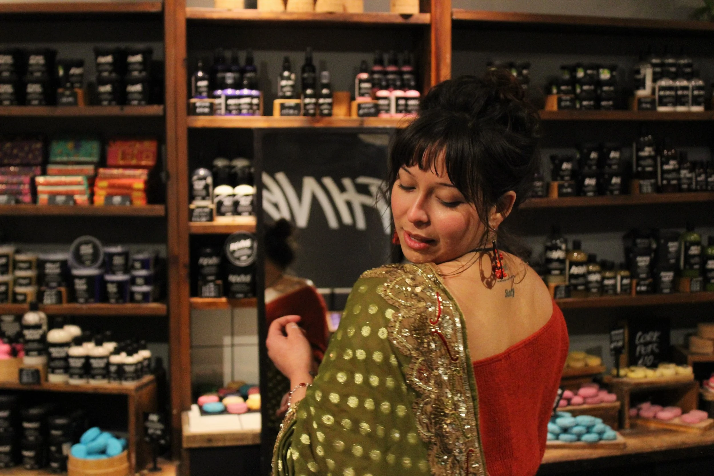 A woman with brown hair wearing a green spotted saree looks over her shoulder
