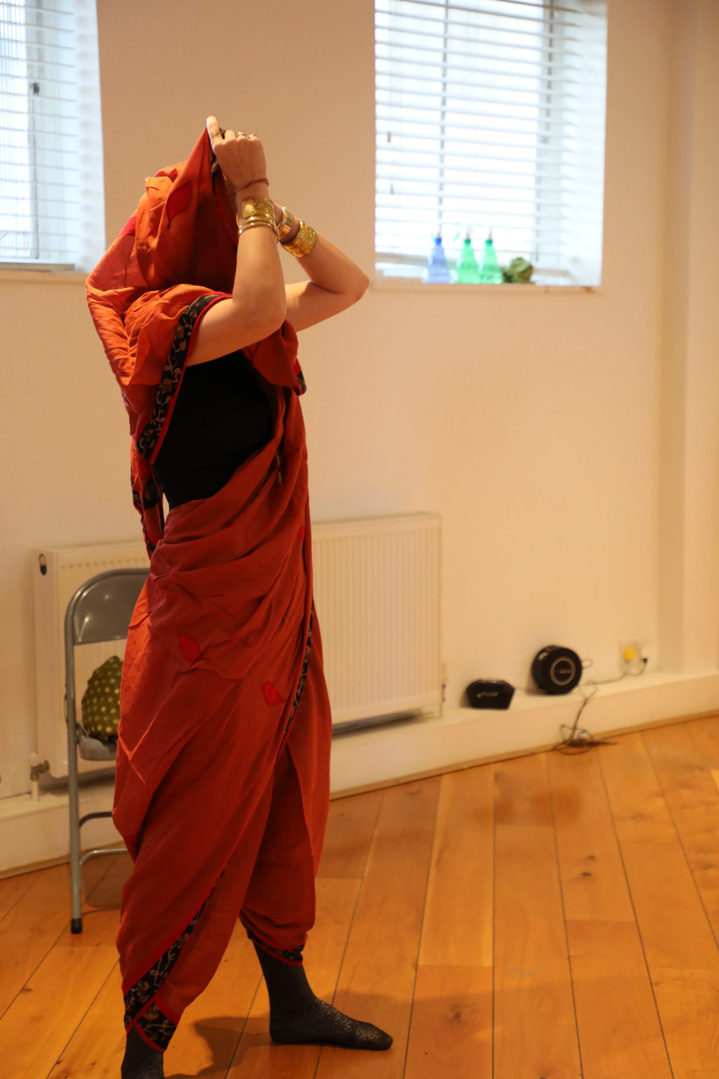 A woman wearing an orange trouser drape saree, draped over her head