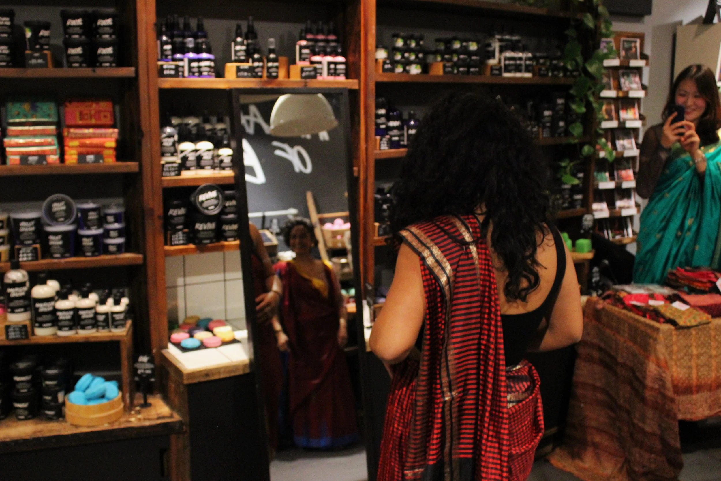 A woman with dark curly hair wearing a burgundy saree looks at her reflection in the mirror
