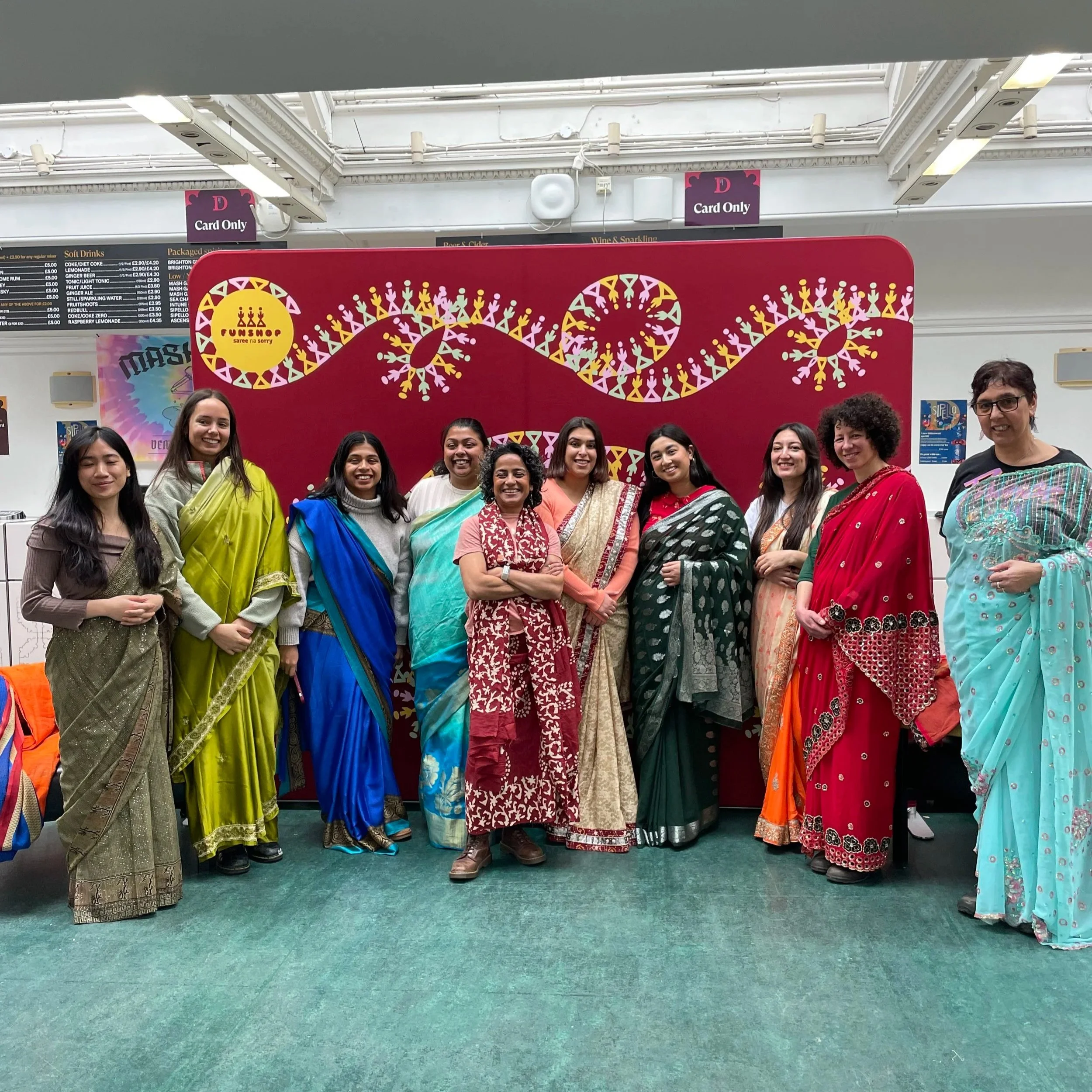 A group of women draped in colourful sarees smiling at the camera