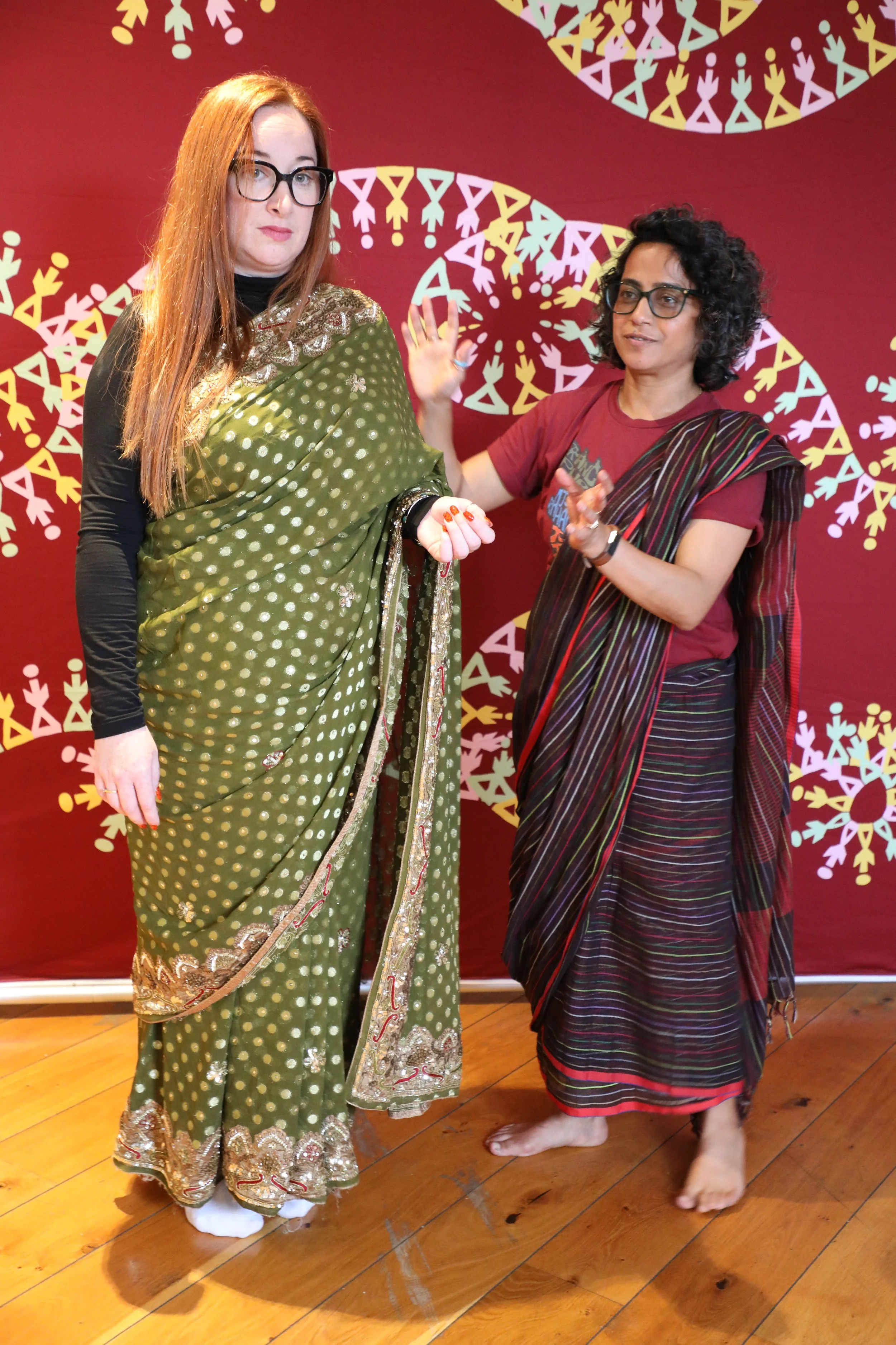 Two women wearing colourful sarees stand together - candid shot, they are not looking at the camera