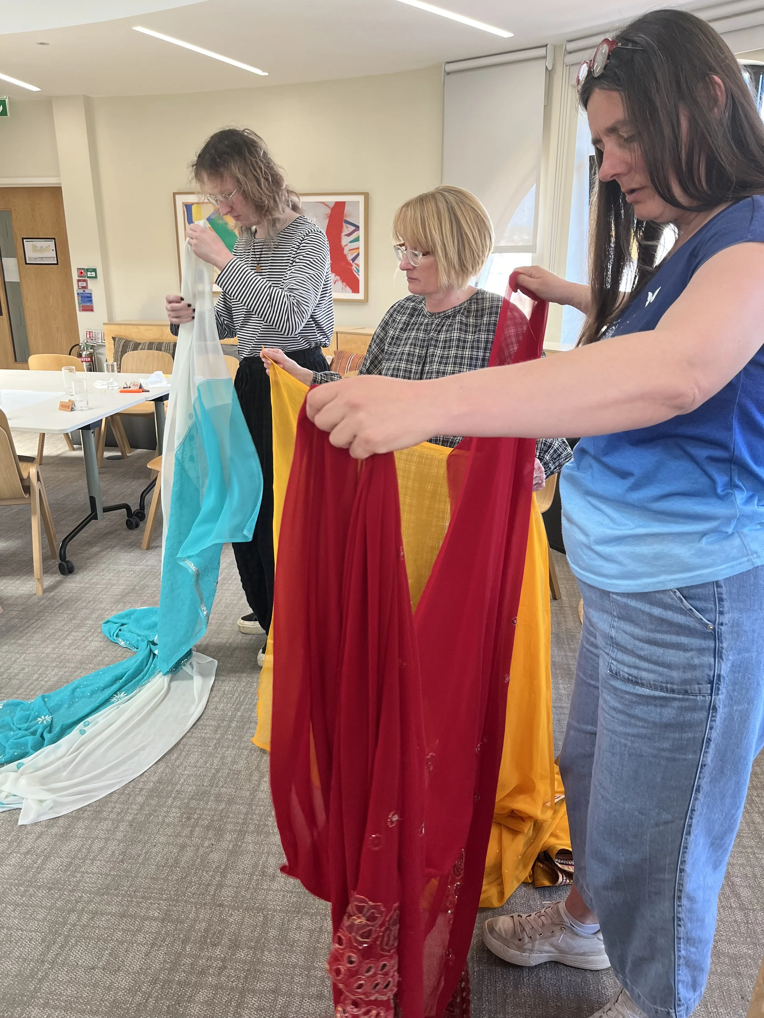 Three women draping colourful sarees on themselves