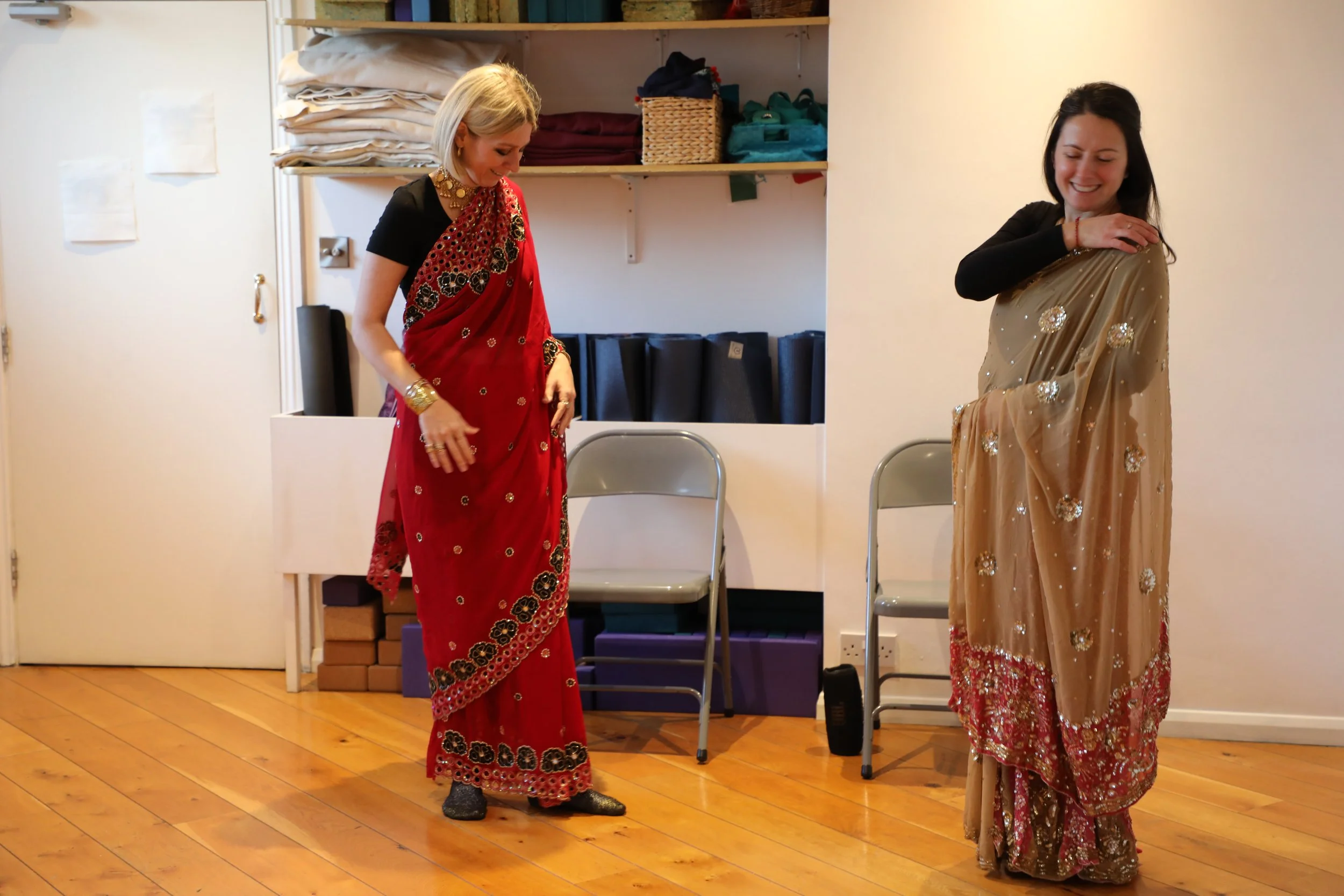 Two white British women wearing colourful sarees stand together, looking away from the camera
