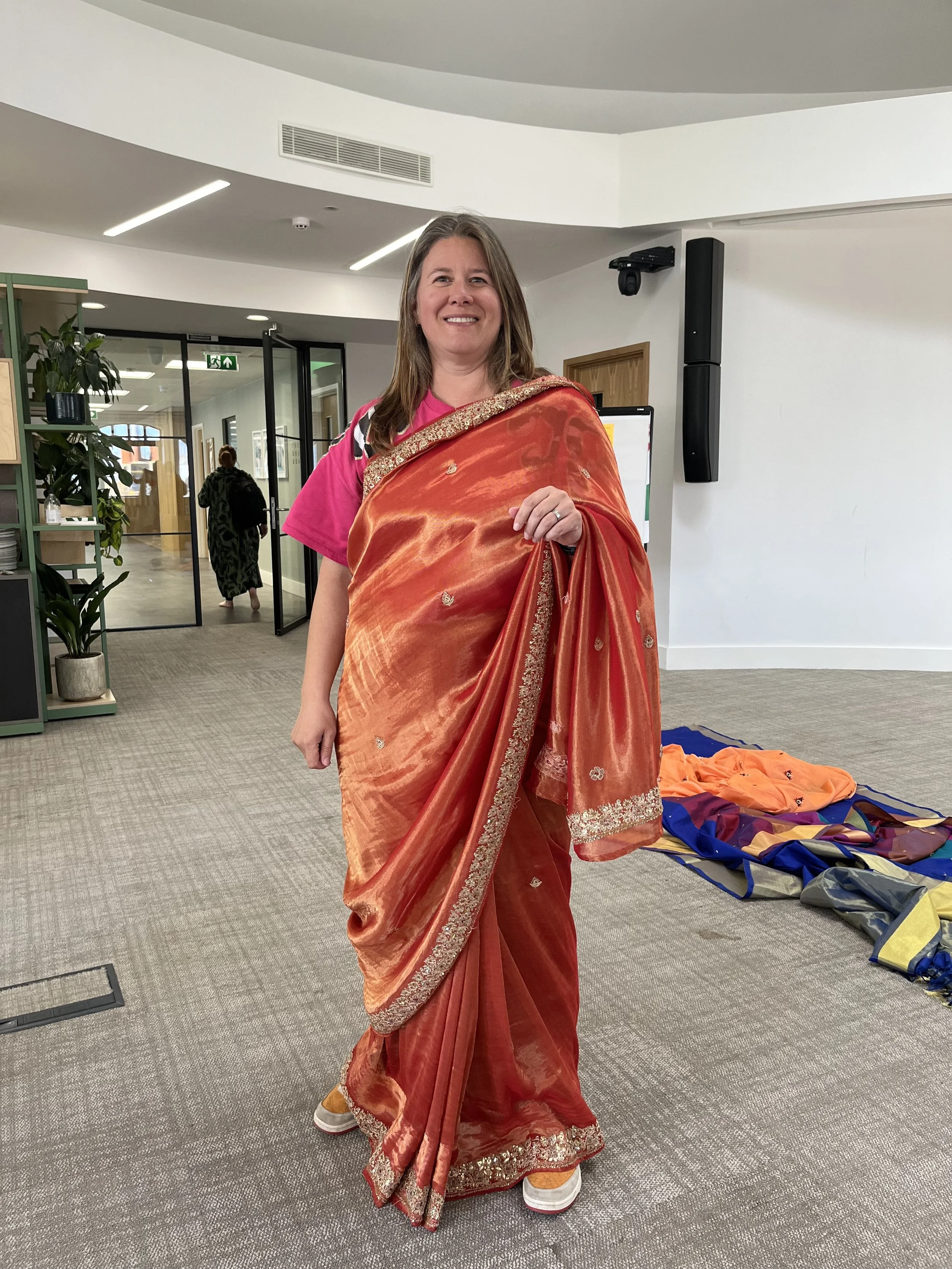 A white-British woman wearing an orange saree smiles at the camera