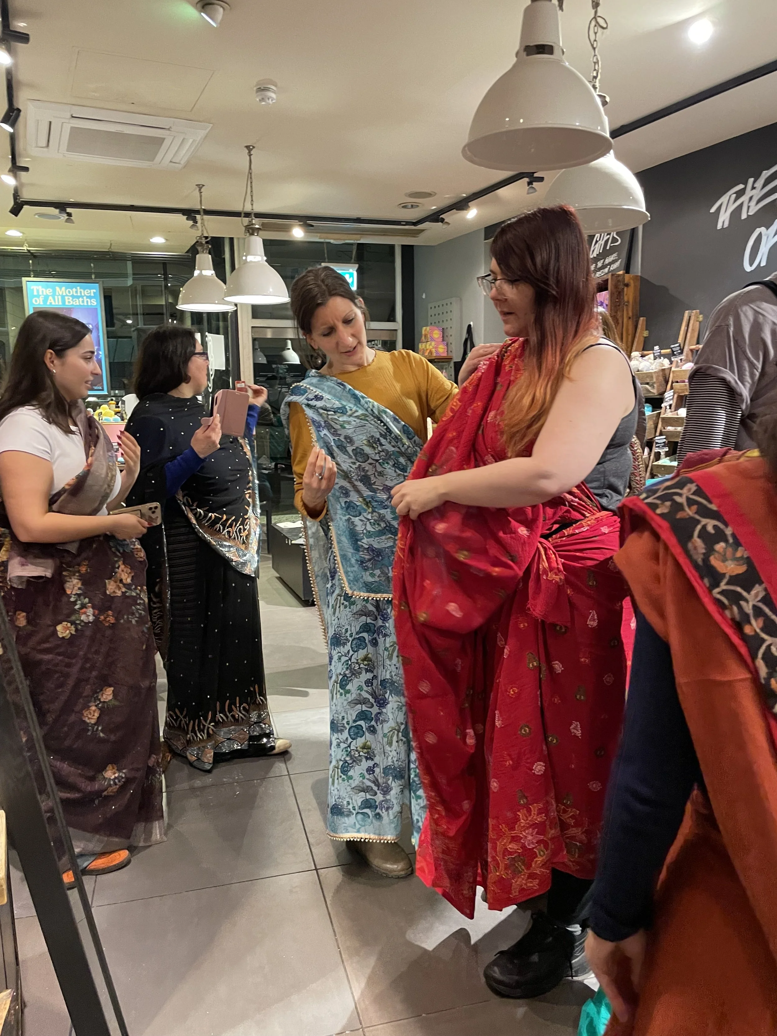 Four women help each other to drape sarees on themselves