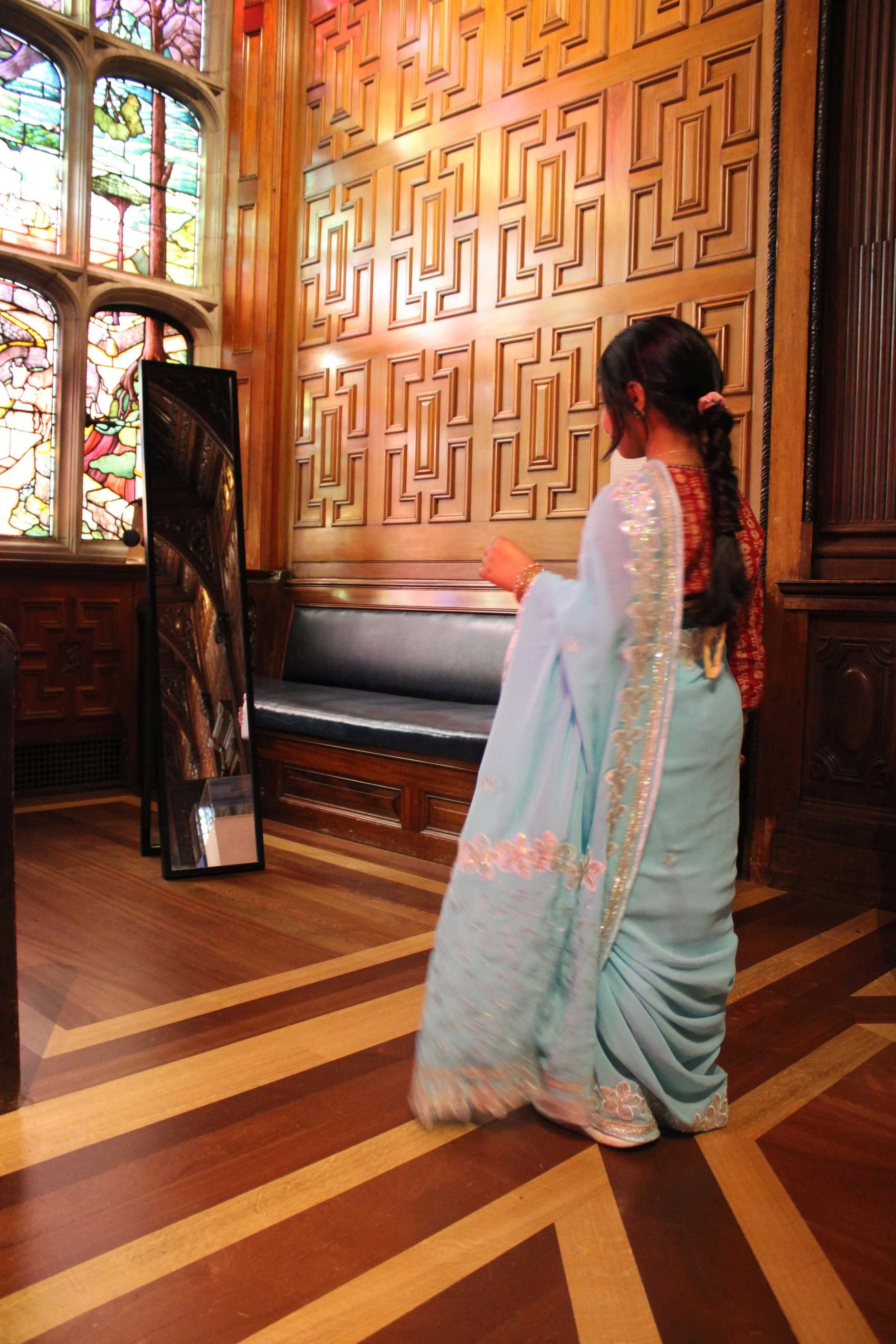 A young South Asian girl wearing a blue saree looks at her reflection in the mirror