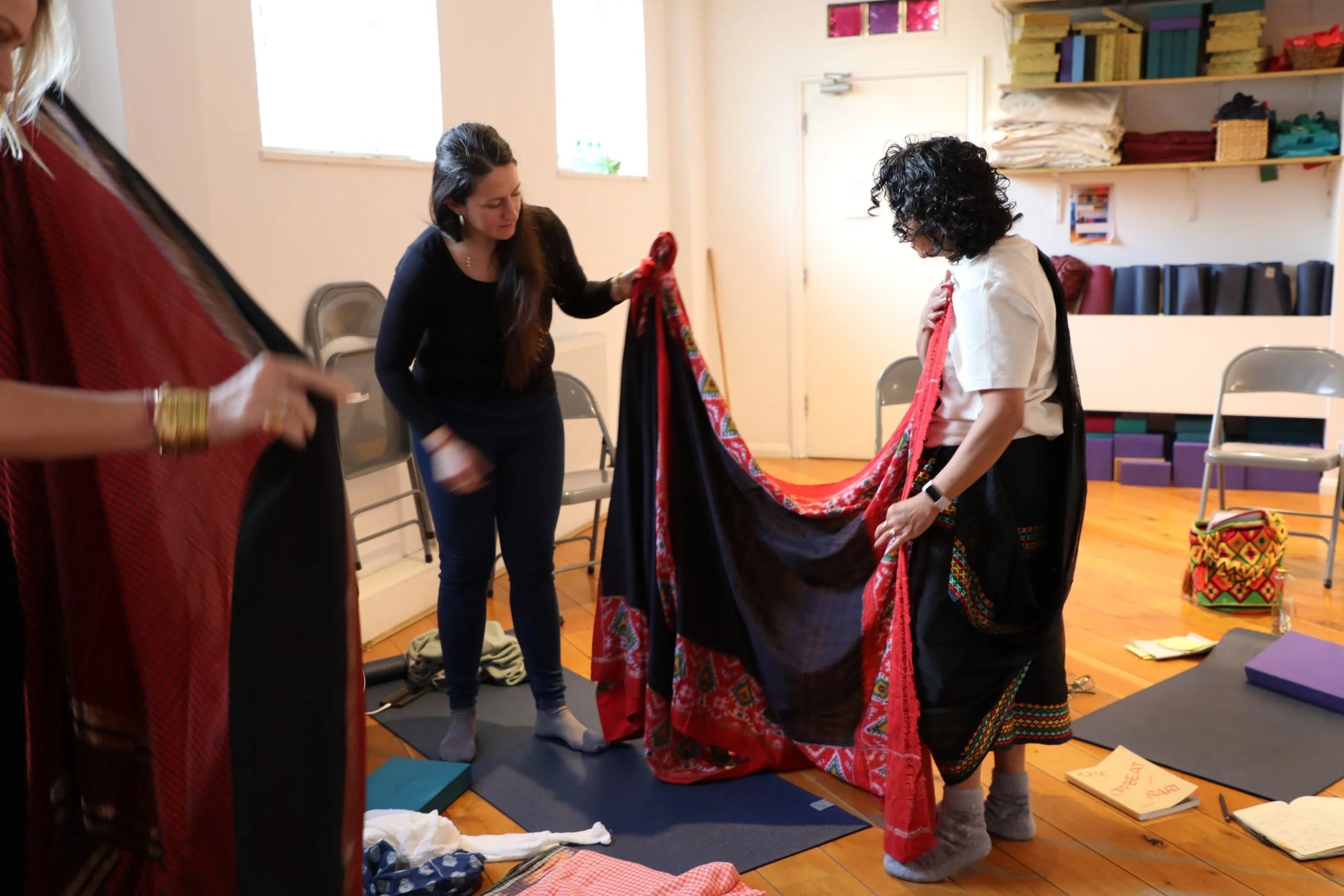 Two women hold a black patterned saree to look at the fabric