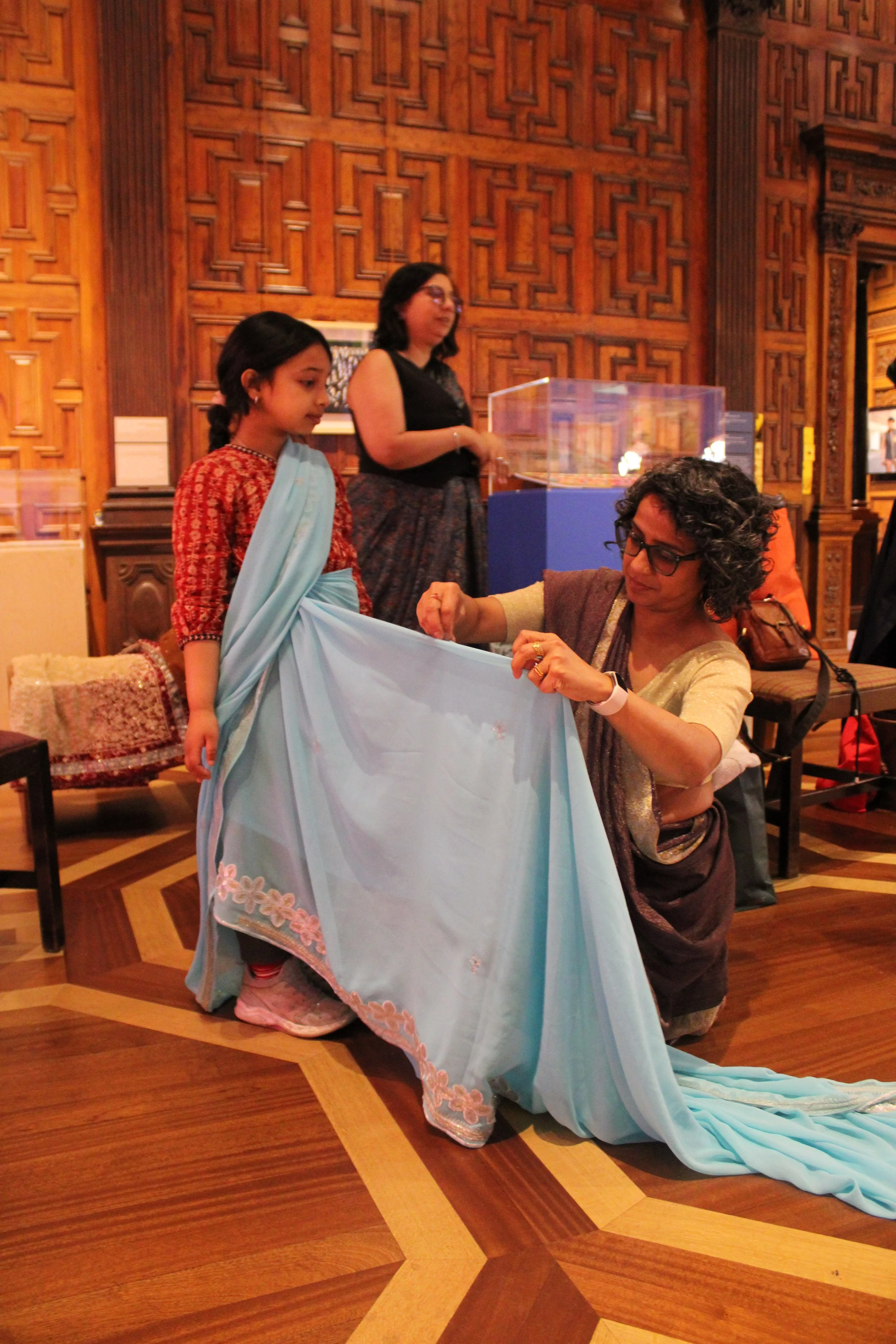 Poppy, a British-Bangladeshi woman, drapes a young Asian girl in a blue saree