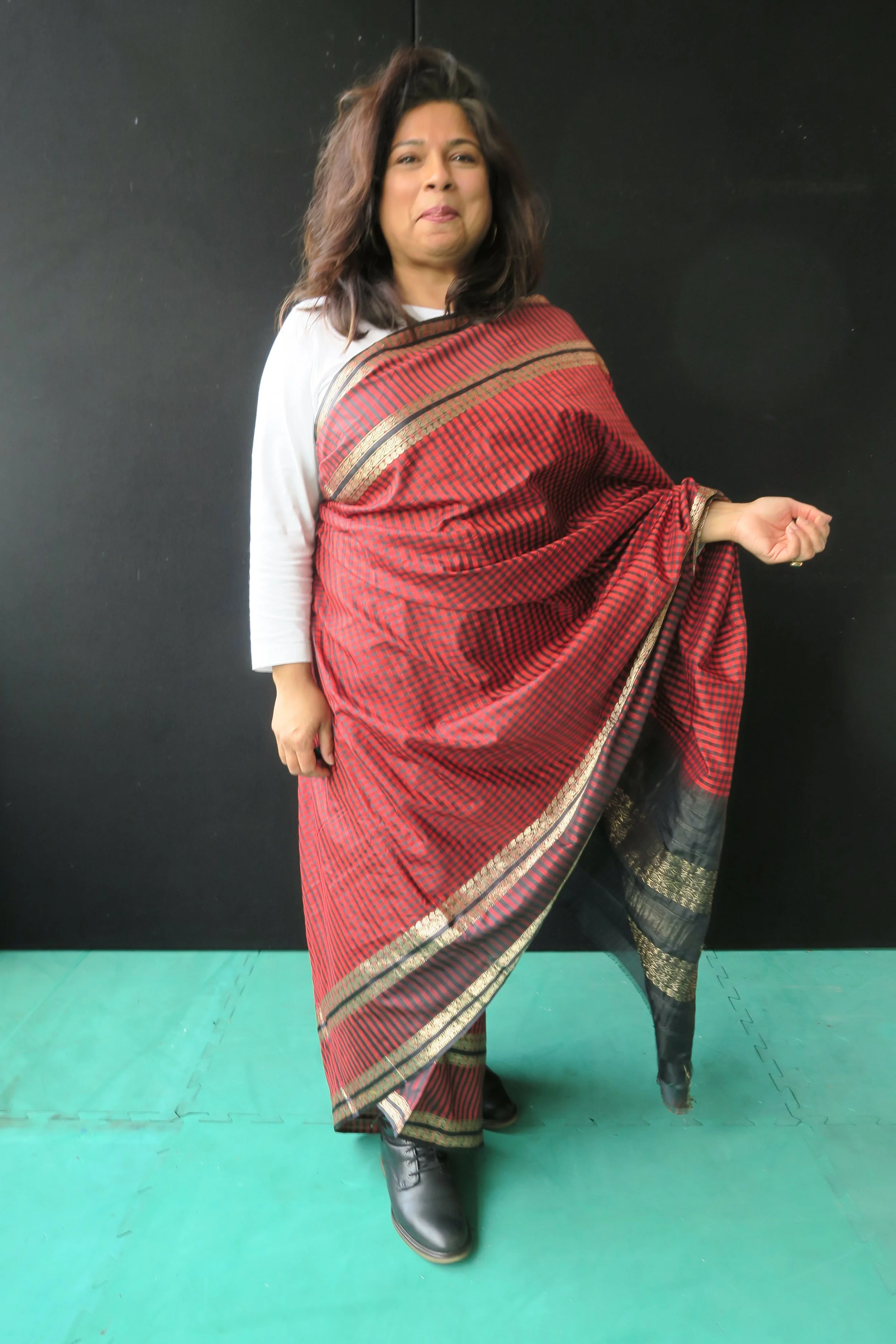 A south asian woman wearing a red saree smiling with one hand out