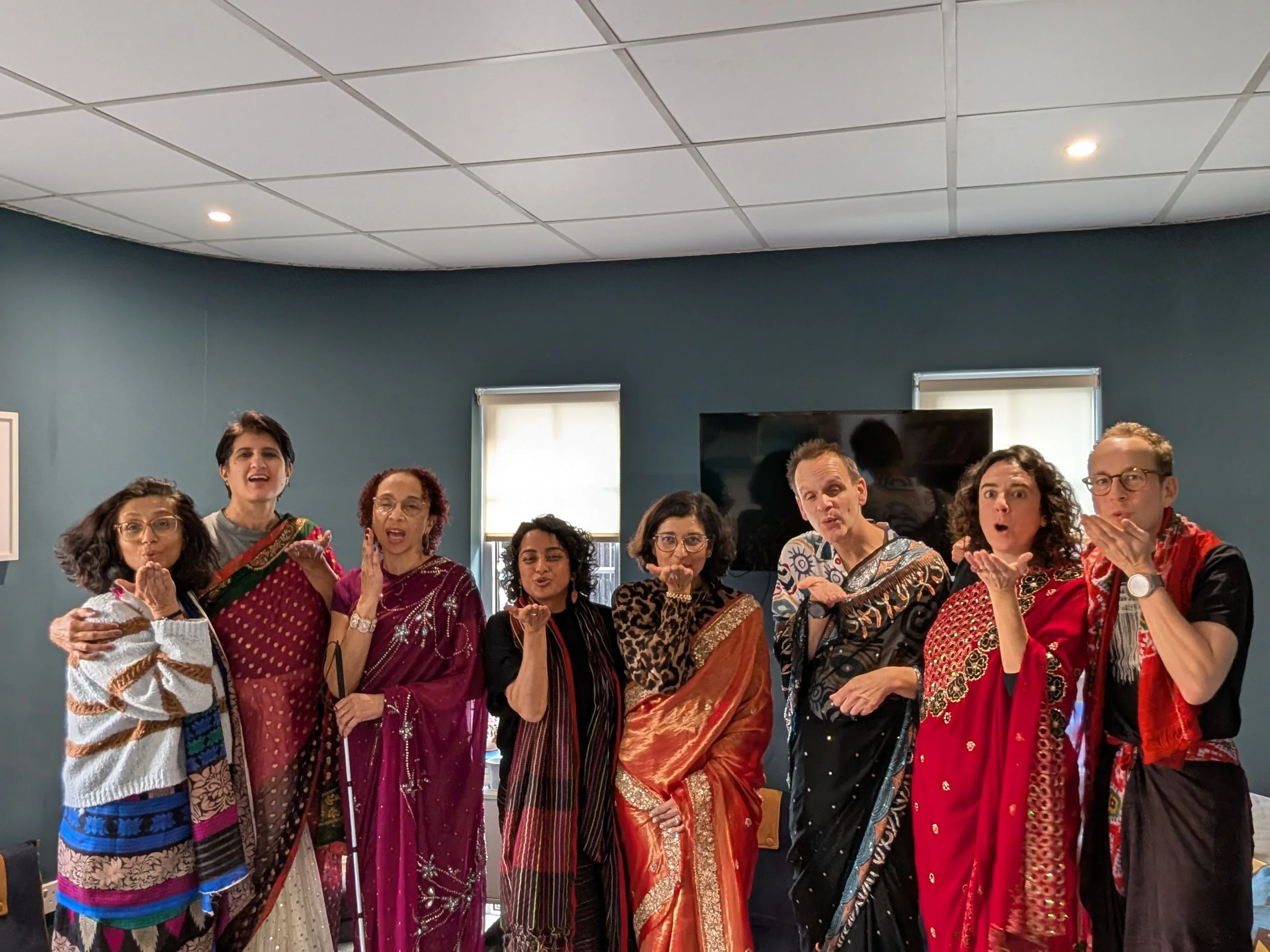 A group of people dressed in sarees blow kisses toward the camera