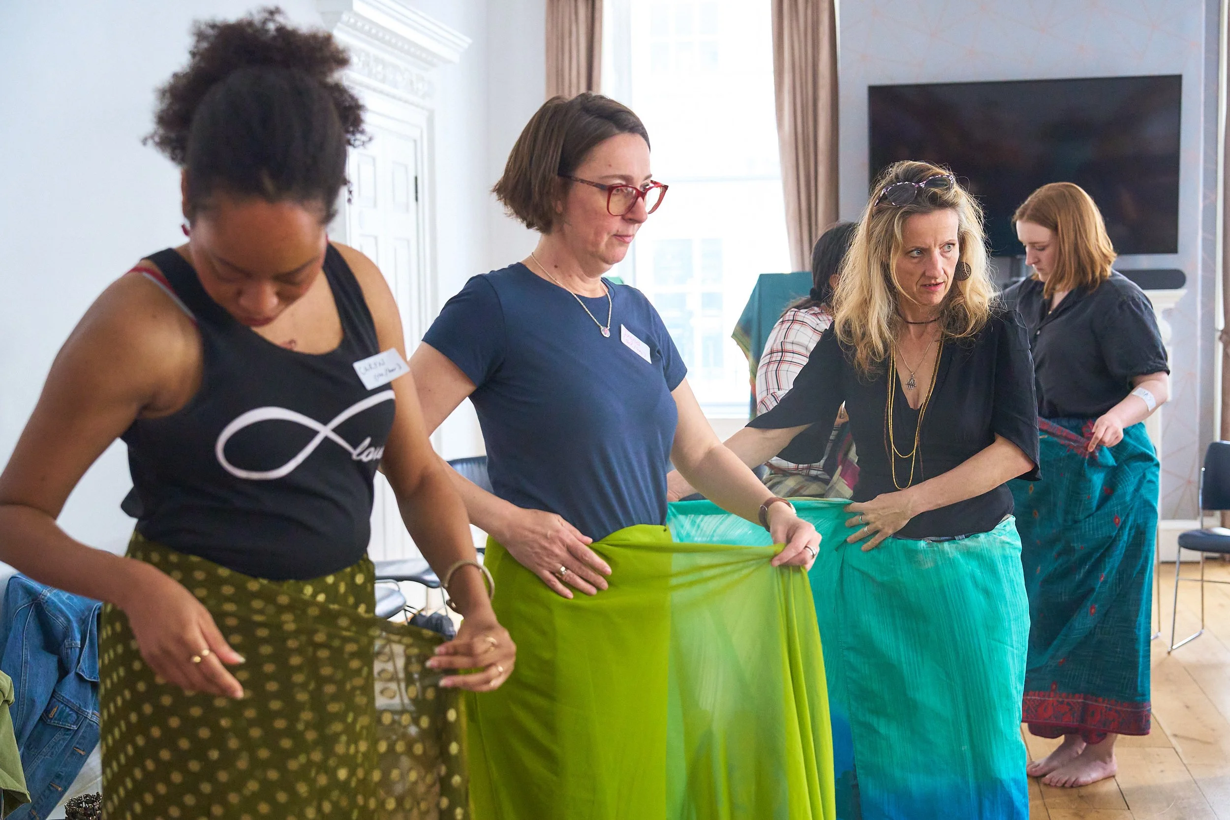 three women drape green sarees of varying shades on themselves