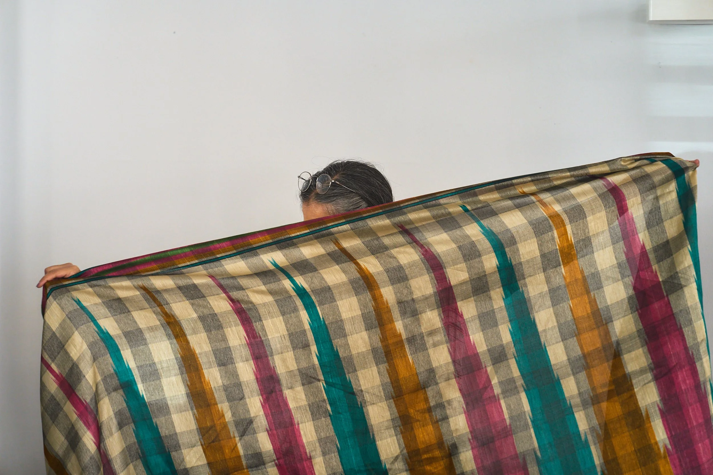 A woman with dark hair holds a patterned saree and stretches it out