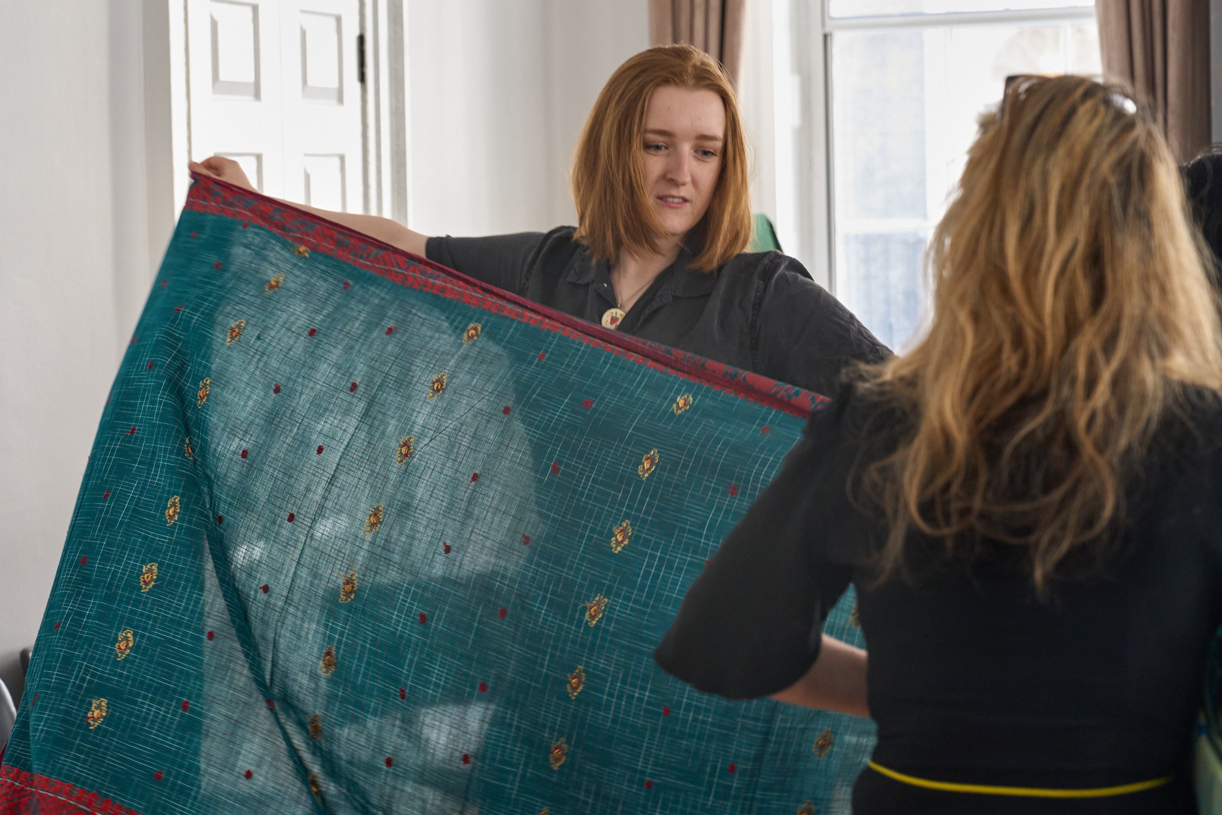 A white-British woman stretches out a green patterned saree in both of her hands