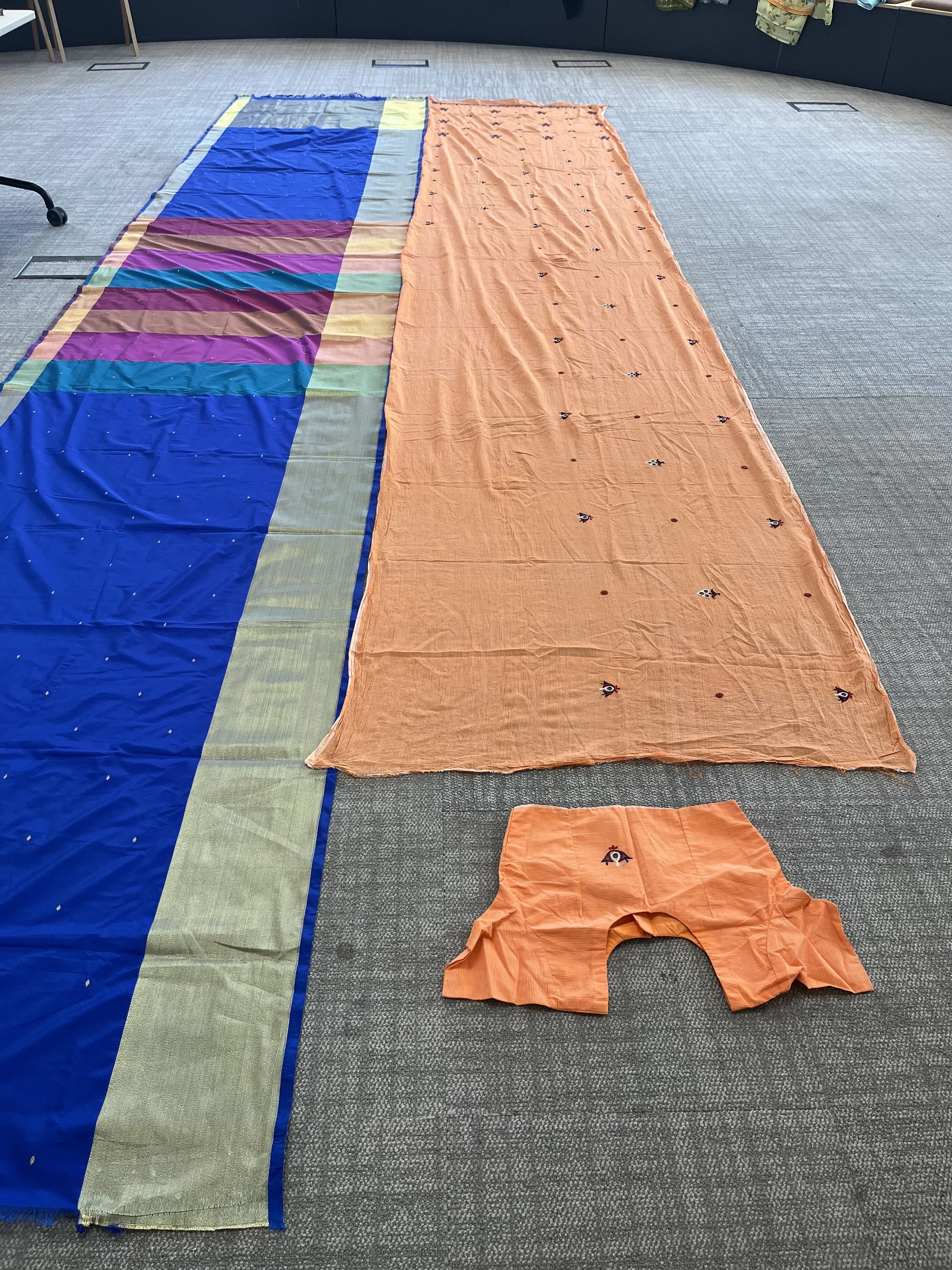 A colourful stripy saree and an orange saree with a blouse laid out on the floor
