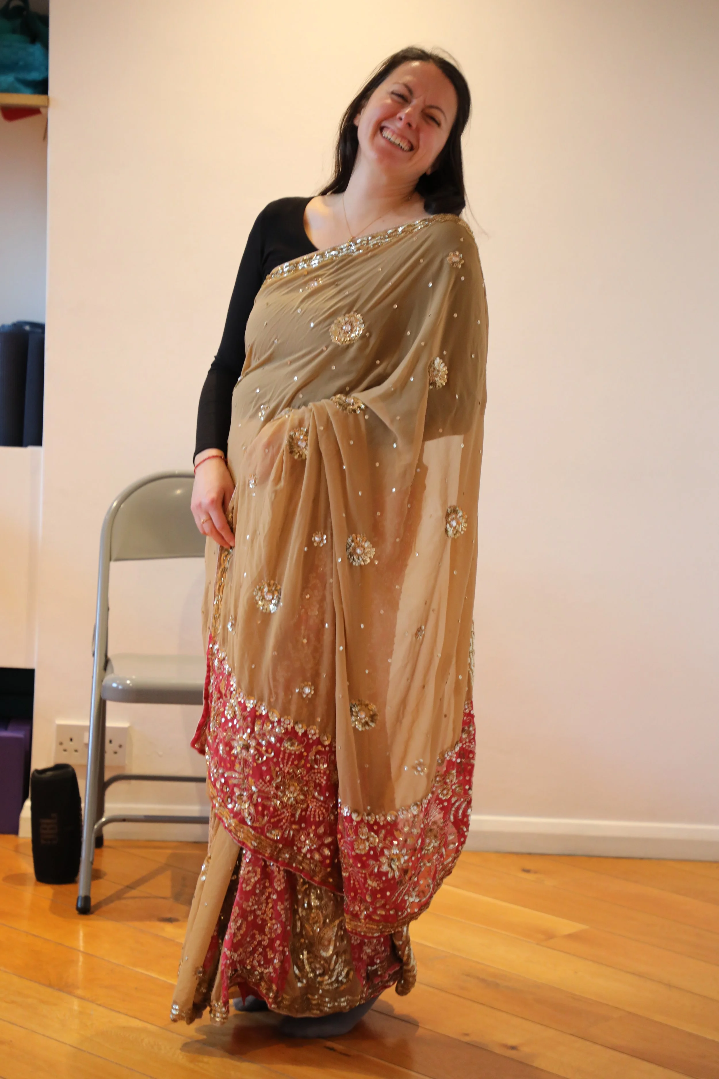 A woman wearing a black top and a gold and pink saree smiles at the camera