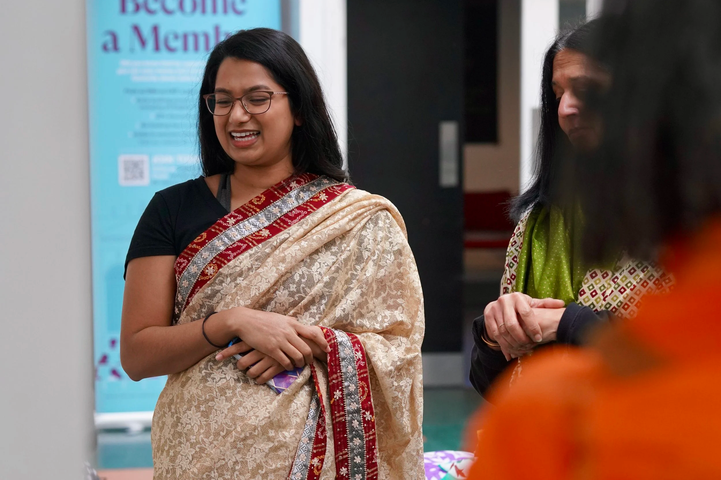 An Asian woman wearing a gold and red saree smiling with her hands crossed