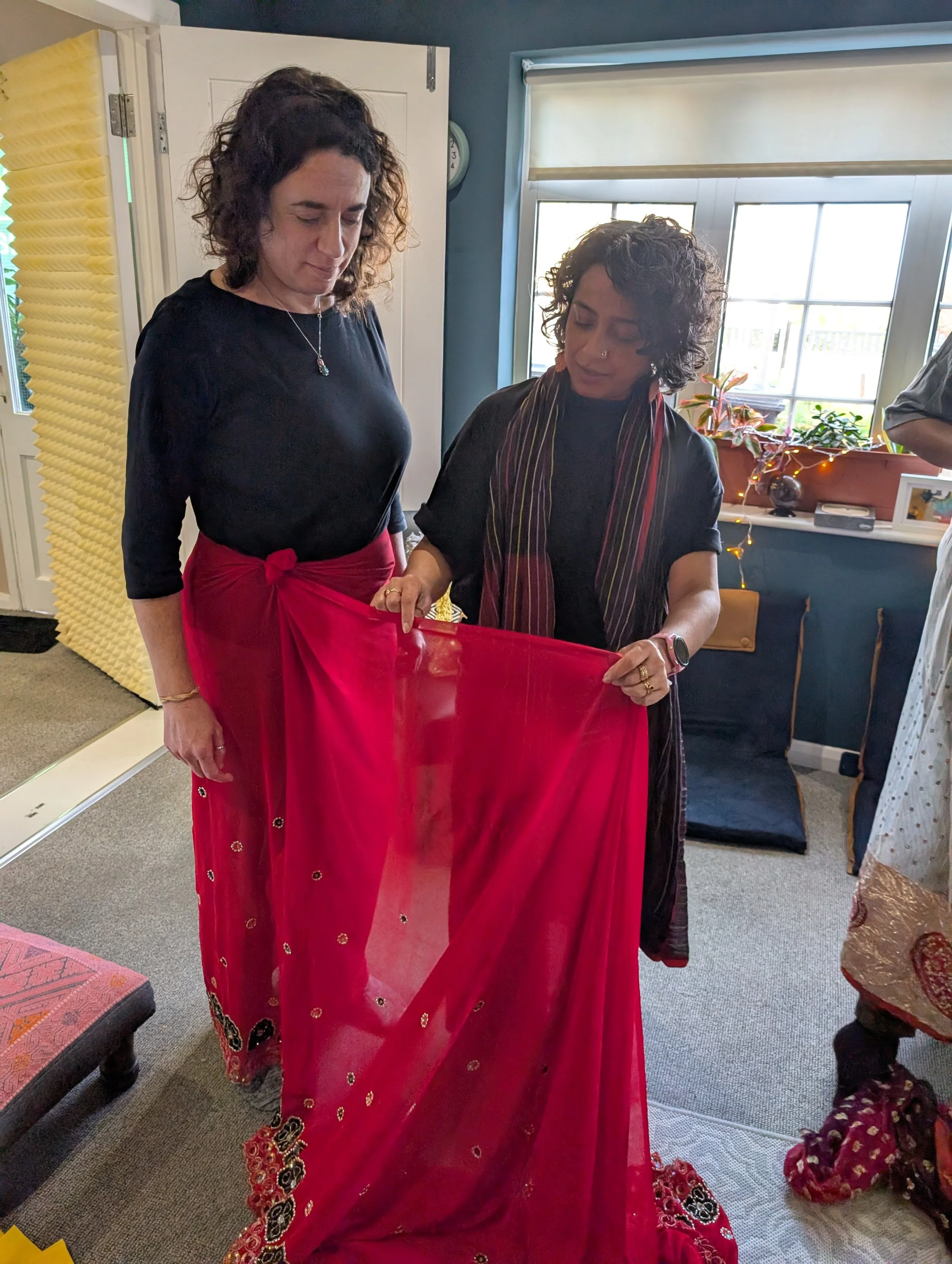 Poppy helps a white British woman to pleat a red patterened saree