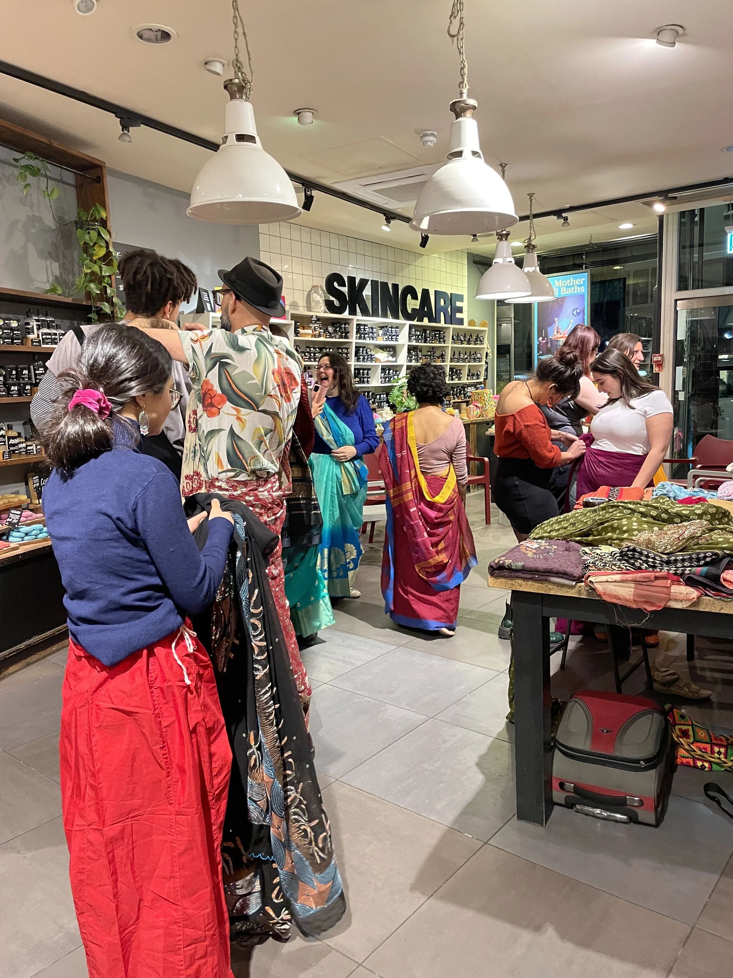 A group of men and women drape themselves in sarees, looking away from the camera