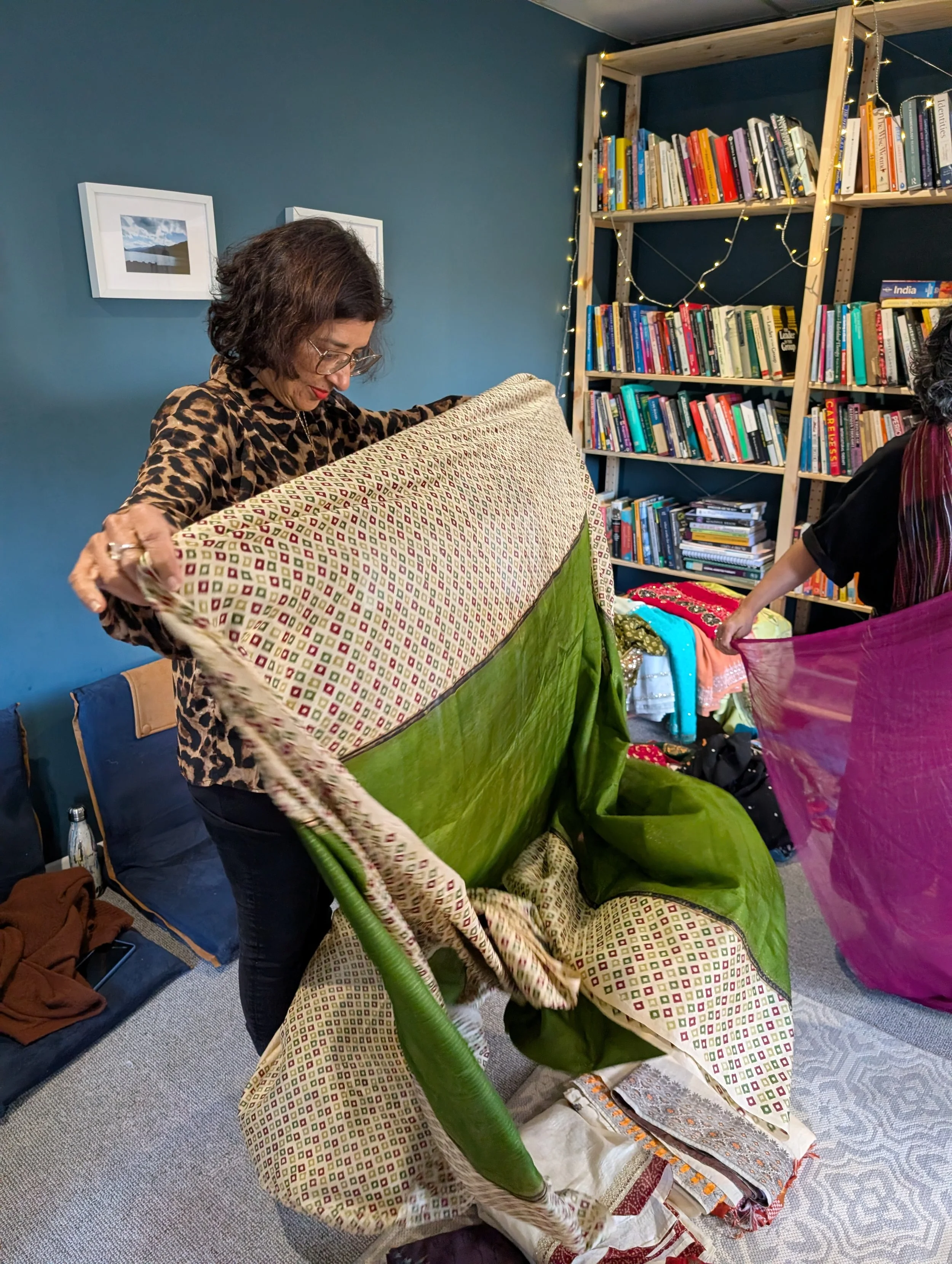 A woman holding up a green patterened saree to drape it on herself