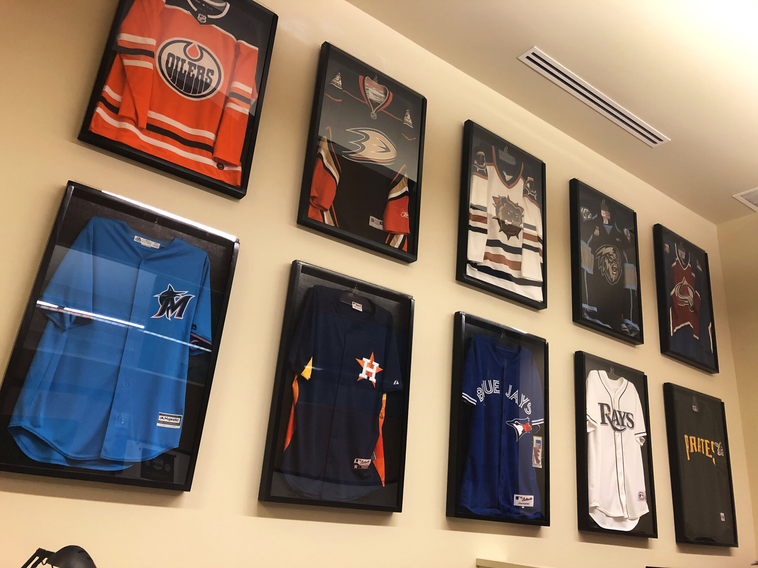 A wall of framed jerseys, each with a different sports team brand identity.
