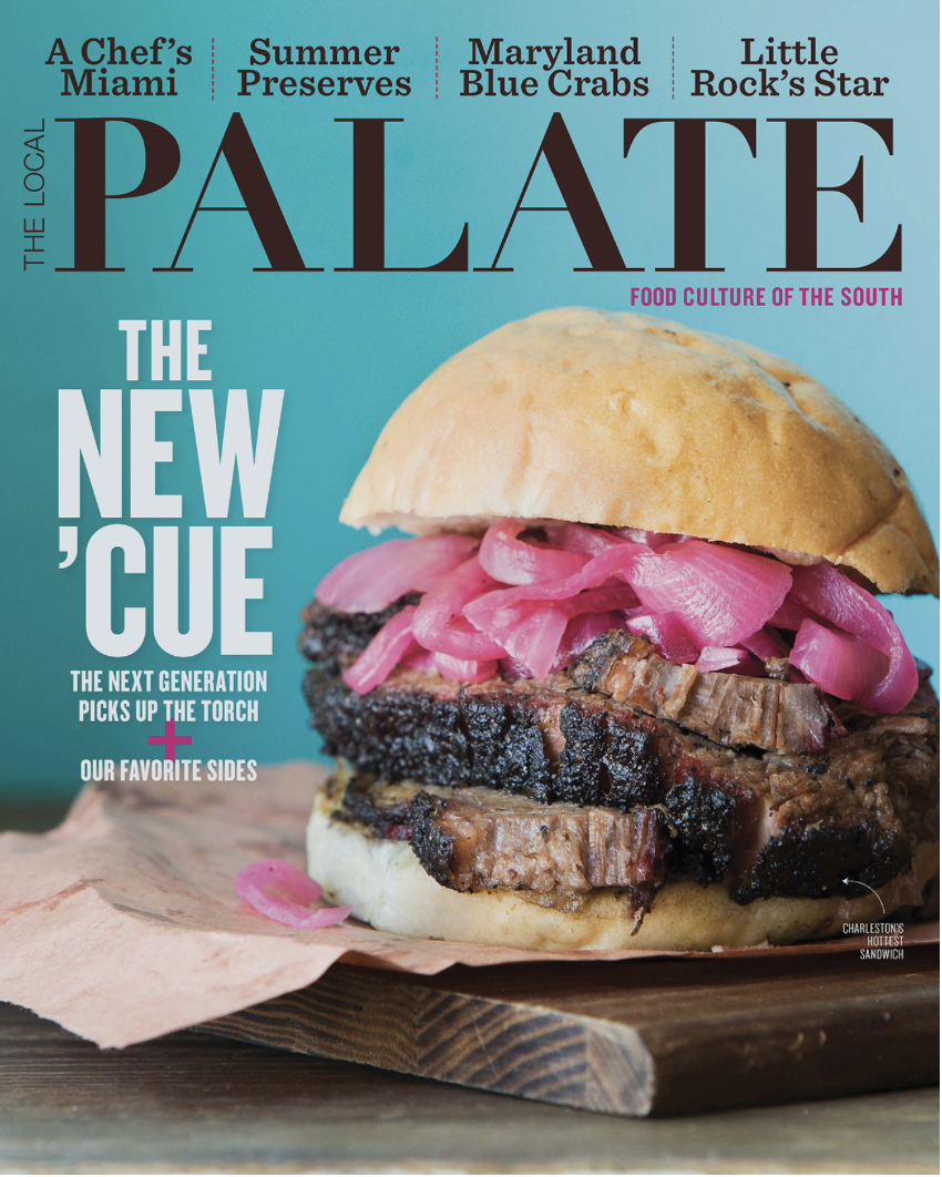 Cover of Palate magazine showcasing a barbecue brisket sandwich with pickled onions on top, placed on a wooden board with paper wrapping, set against a turquoise background.