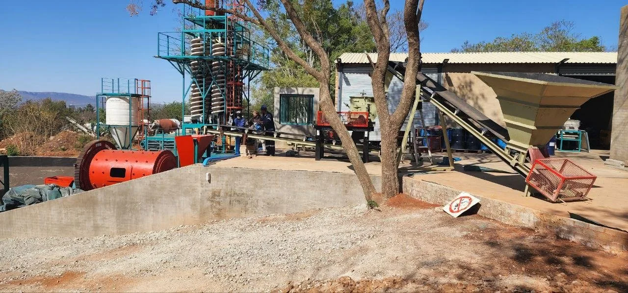 Industrial outdoor scene with machinery, a small building, and a tree, under clear blue sky.