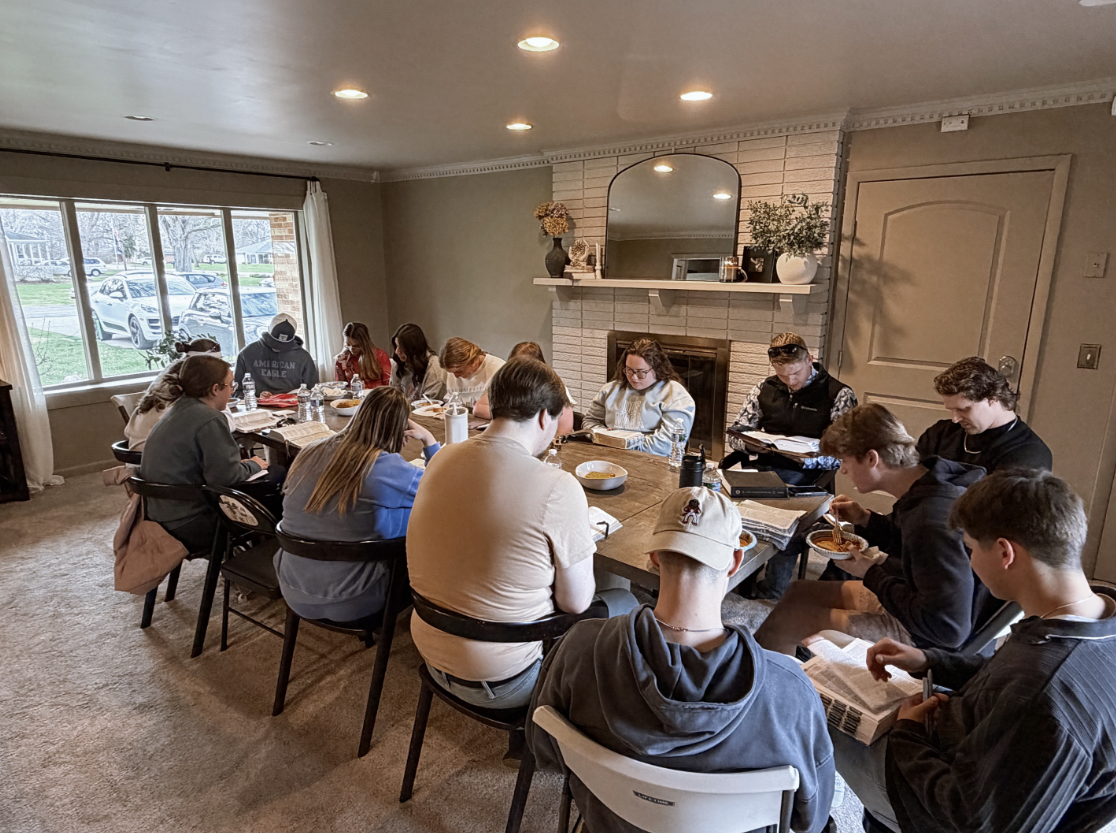 Young adults sitting around a table in a home, studying the Bible in community. 