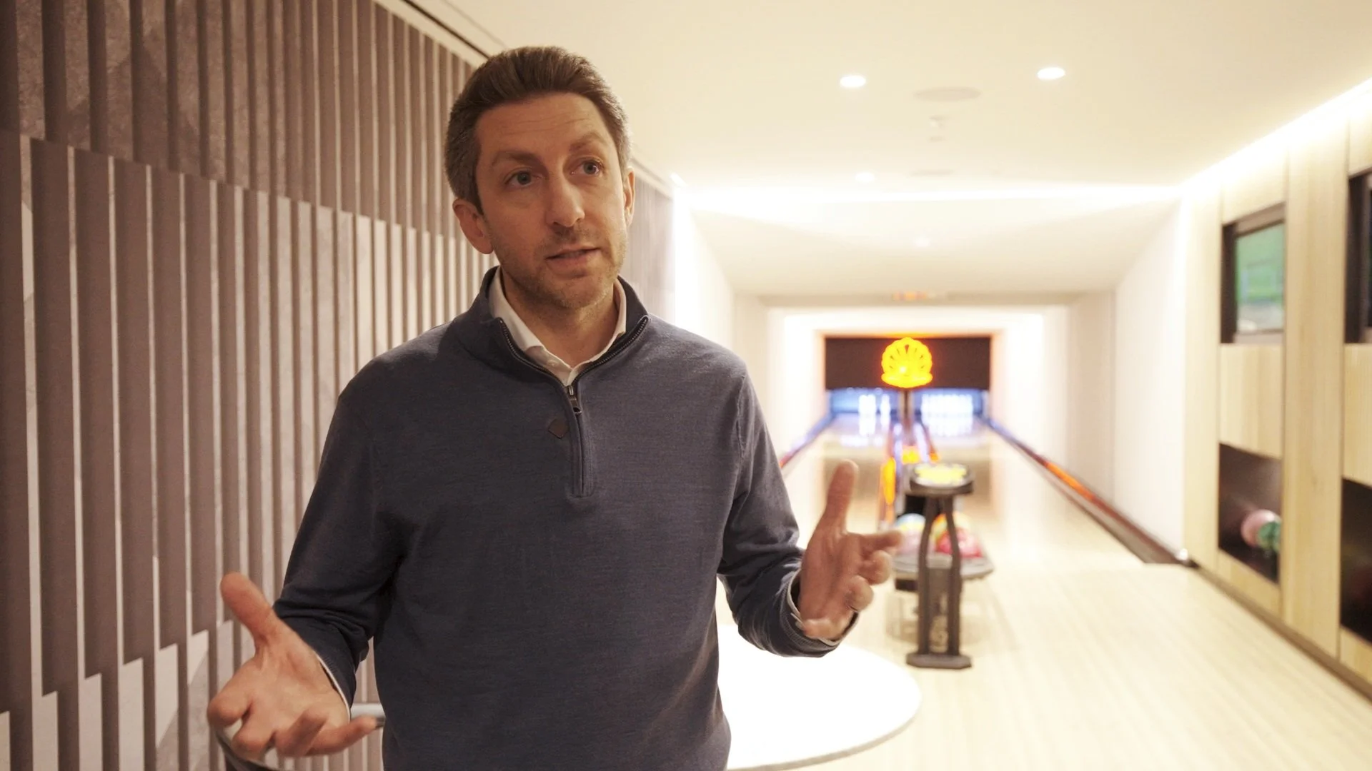 Joey Chilelli speaking during an interview in a modern, well-lit bowling alley featuring wooden lanes in Manhattan's former Pearl House, contemporary design elements, and ambient lighting