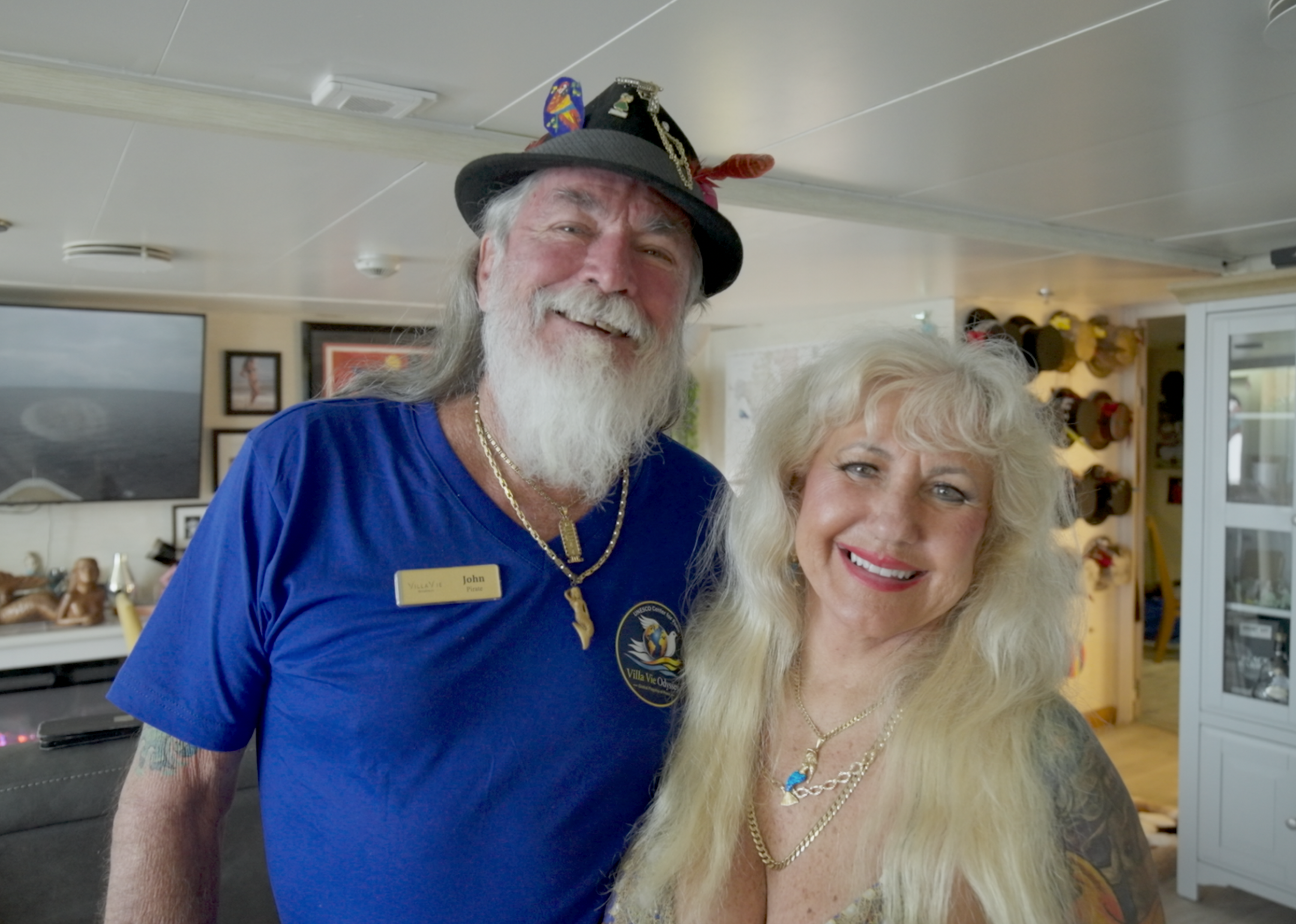 Melody and John Hennessee in their cabin aboard the MS Odyssey with hat collection behind them
