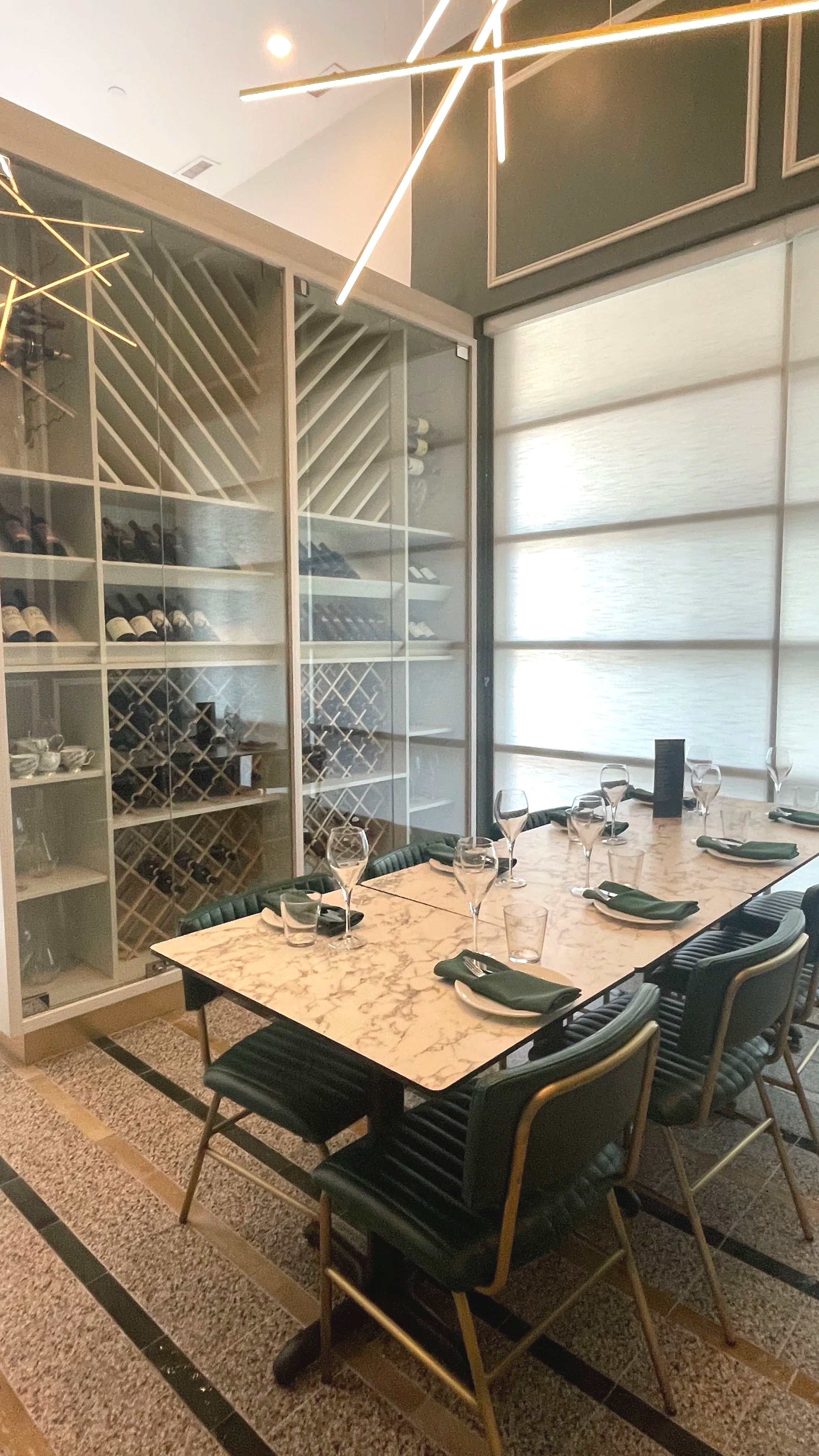 Elegant dining room with a marble table set with glasses and napkins, surrounded by black chairs, and a glass wine rack with bottles in the background.