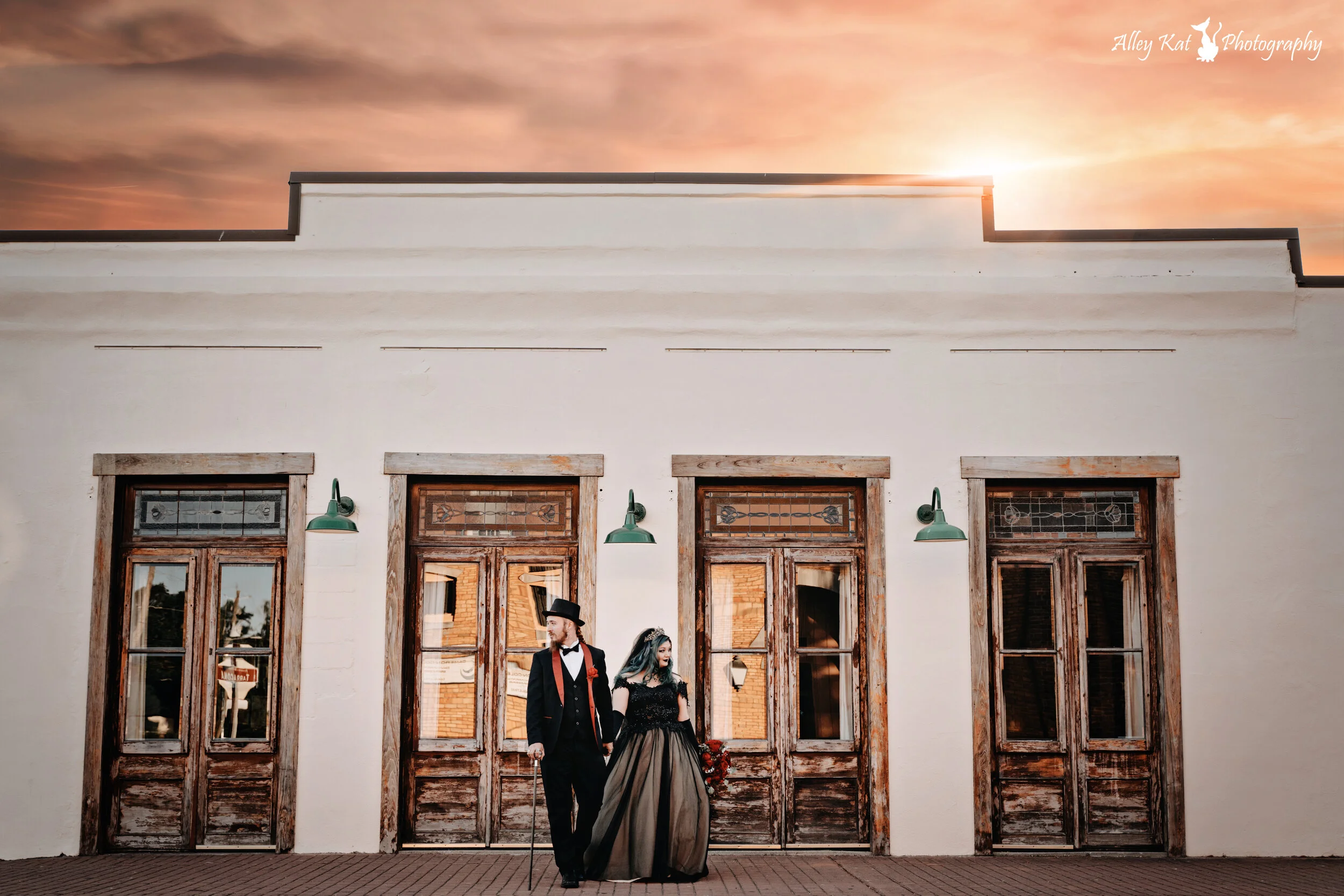 A couple dressed in vintage attire walking hand in hand in front of a white building with four wooden doors, during sunset. Pensacola wedding photography - pensacola wedding photographer