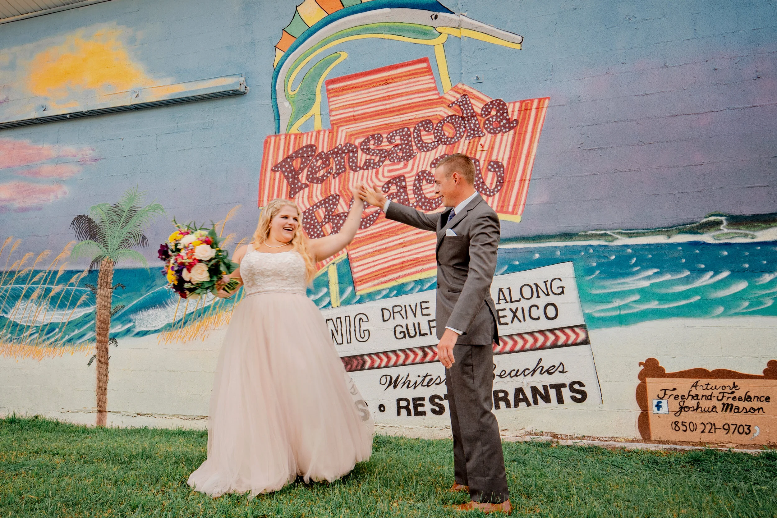 A bride and groom celebrating in front of a colorful mural of a vintage postcard, with the bride holding a bouquet and smiling as they high five. Pensacola wedding photography - pensacola wedding photographer