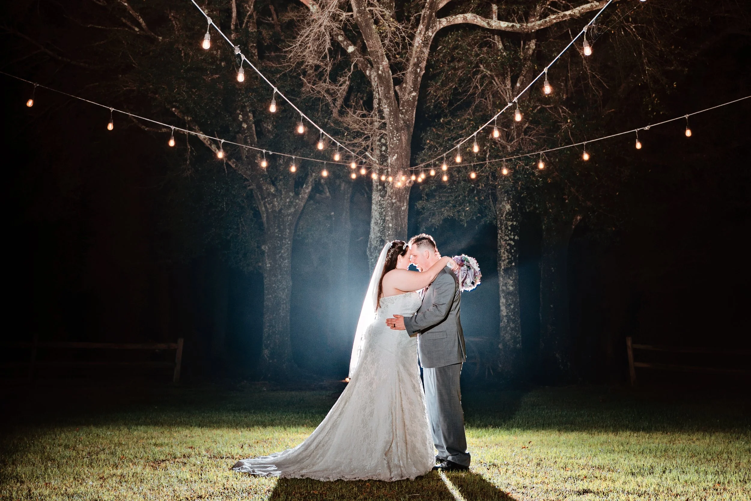 A bride and groom share a kiss during their wedding at night, illuminated by string lights hanging from trees Pensacola wedding photography - pensacola wedding photographer