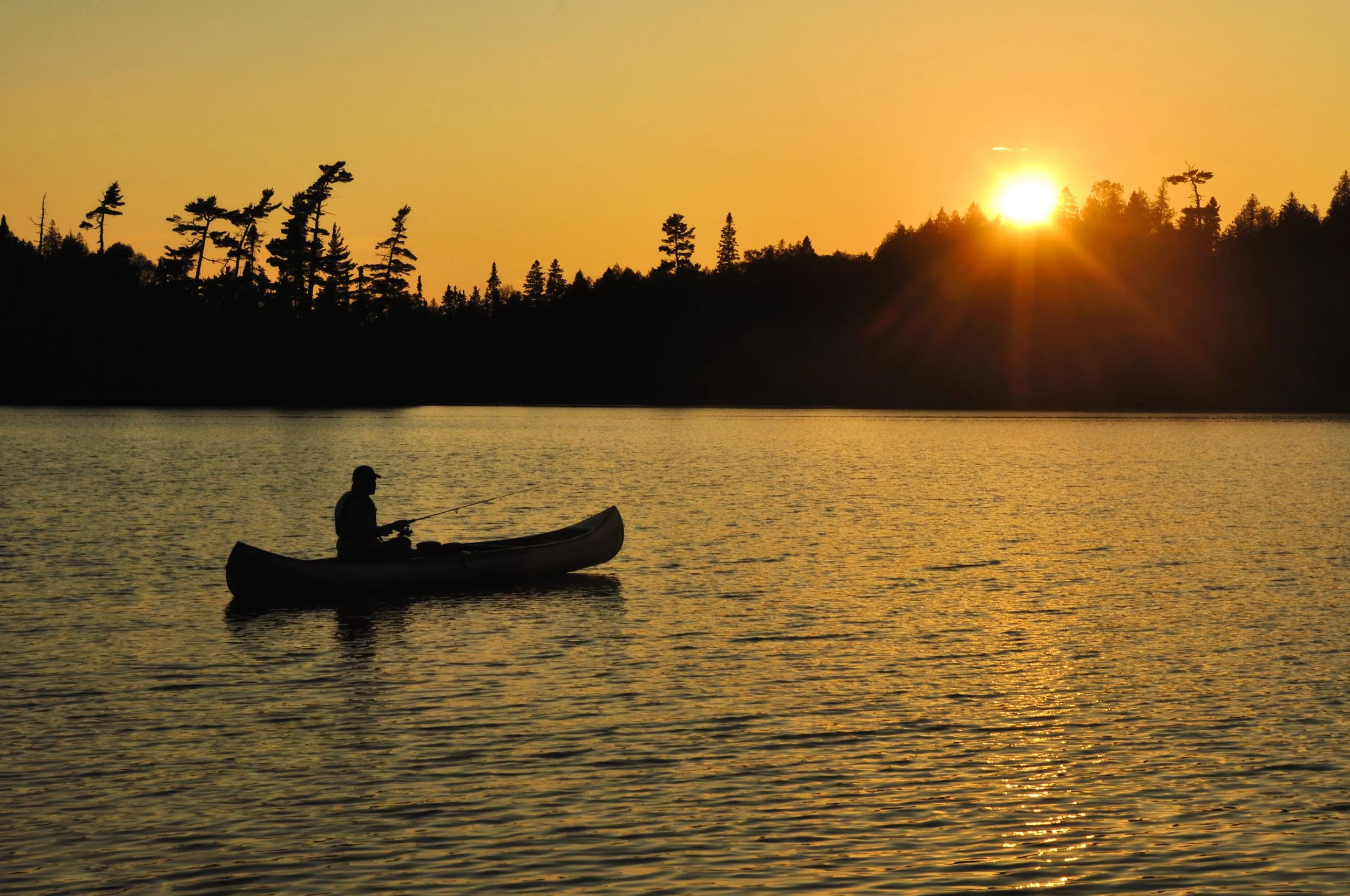 Fisherman paddling a canoe across a calm Minnesota lake at sunrise, reflecting the outdoor lifestyle and adventure behind Wolf Creek's everyday field watches.