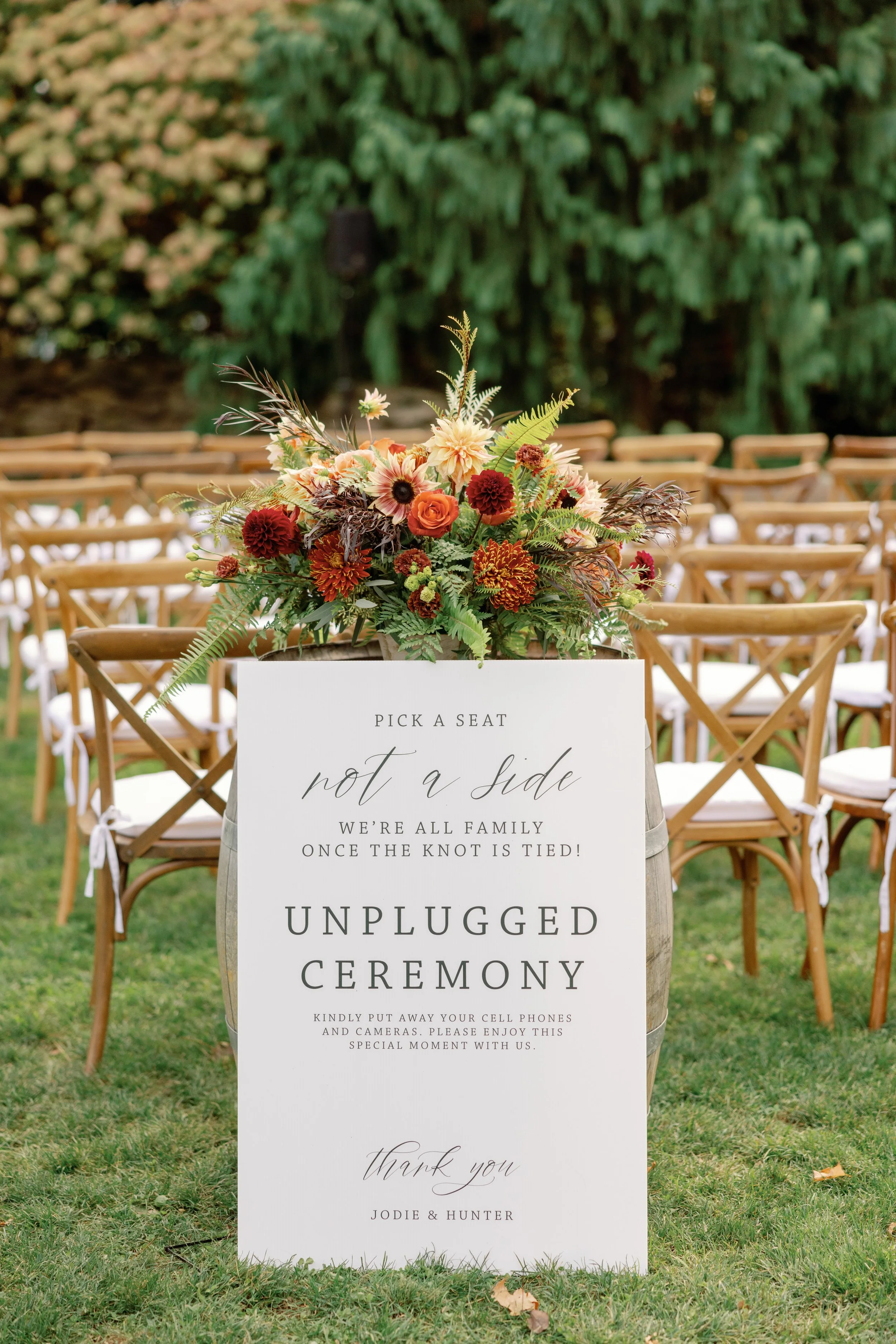 Ivory unplugged ceremony sign reading Pick a Seat, Not a Side, displayed on a whiskey barrel with autumn florals at Kalmia Garden at Gastler Farm in Durham, Connecticut.