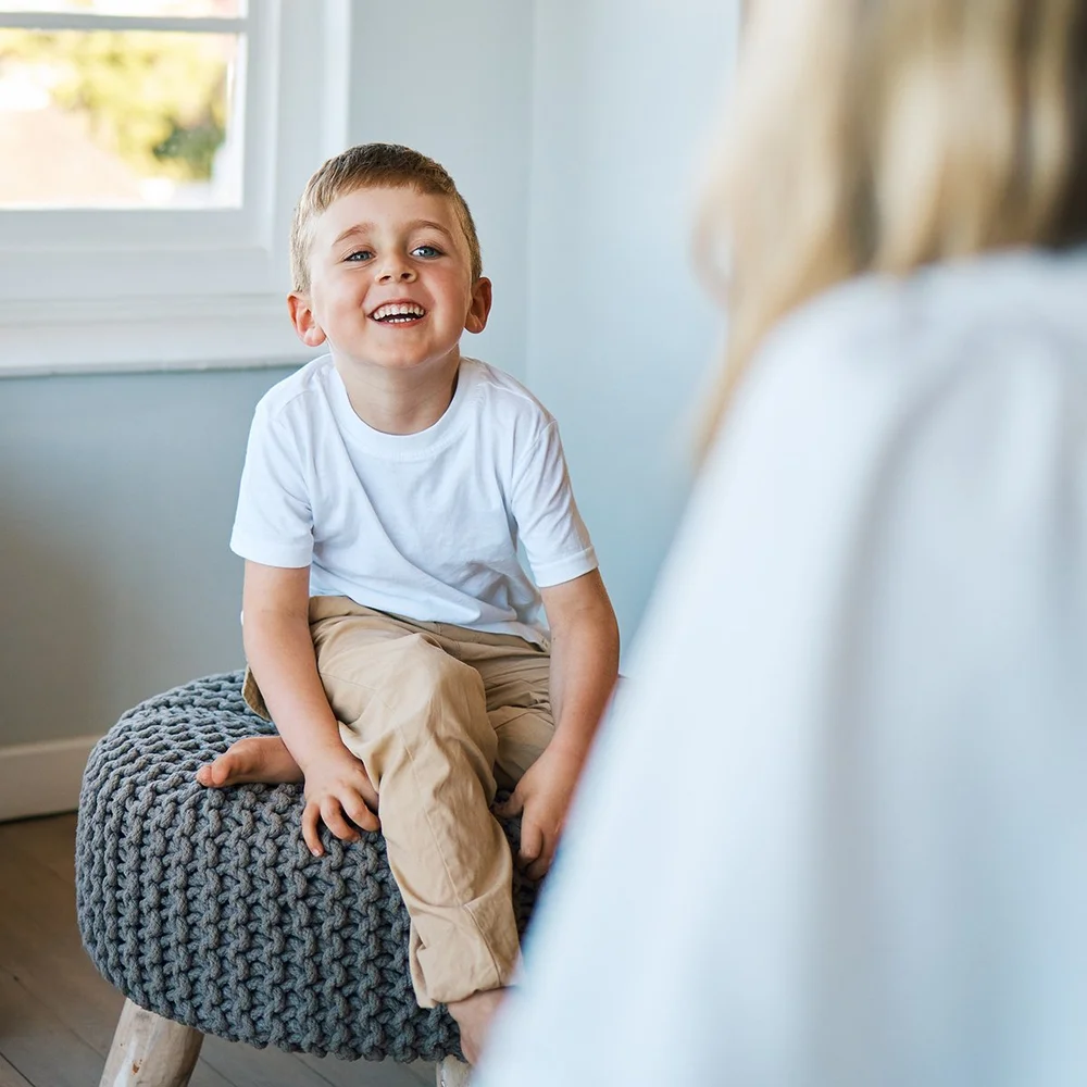 A smiling young boy sitting during an ABA therapy session with his therapist