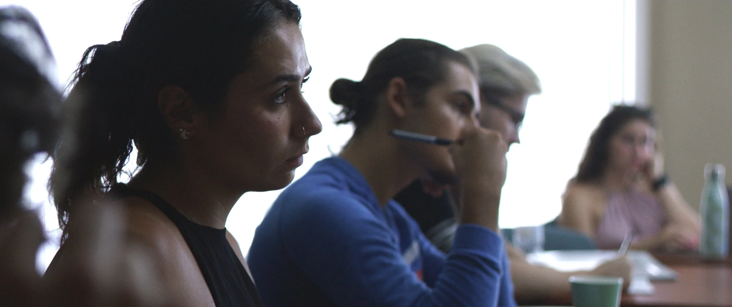 People sitting at a conference table attentively listening, with one person taking notes, in a professional setting.