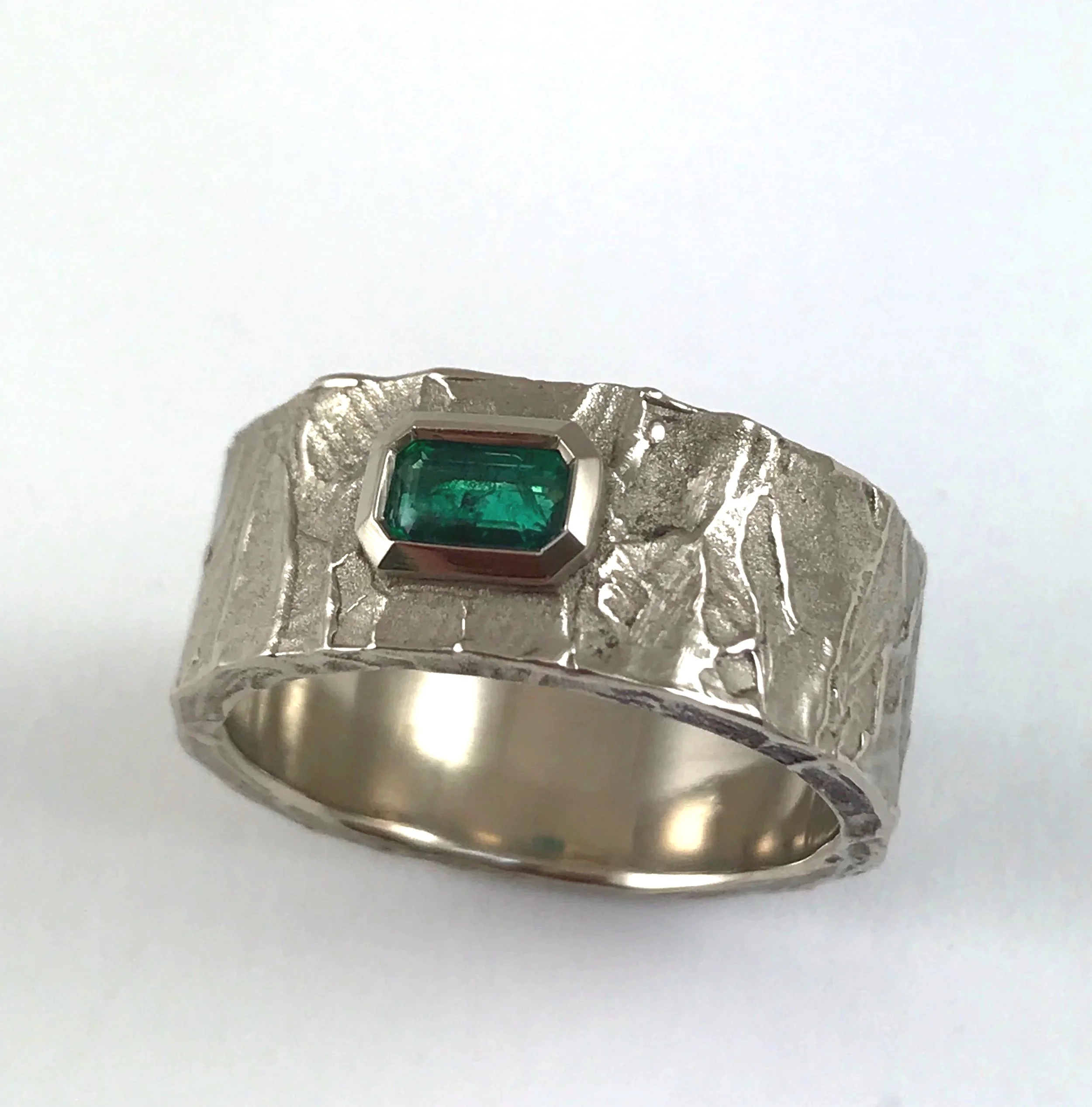 For Michael. The wide textured band holds his emerald in a bezel of 18KPW.