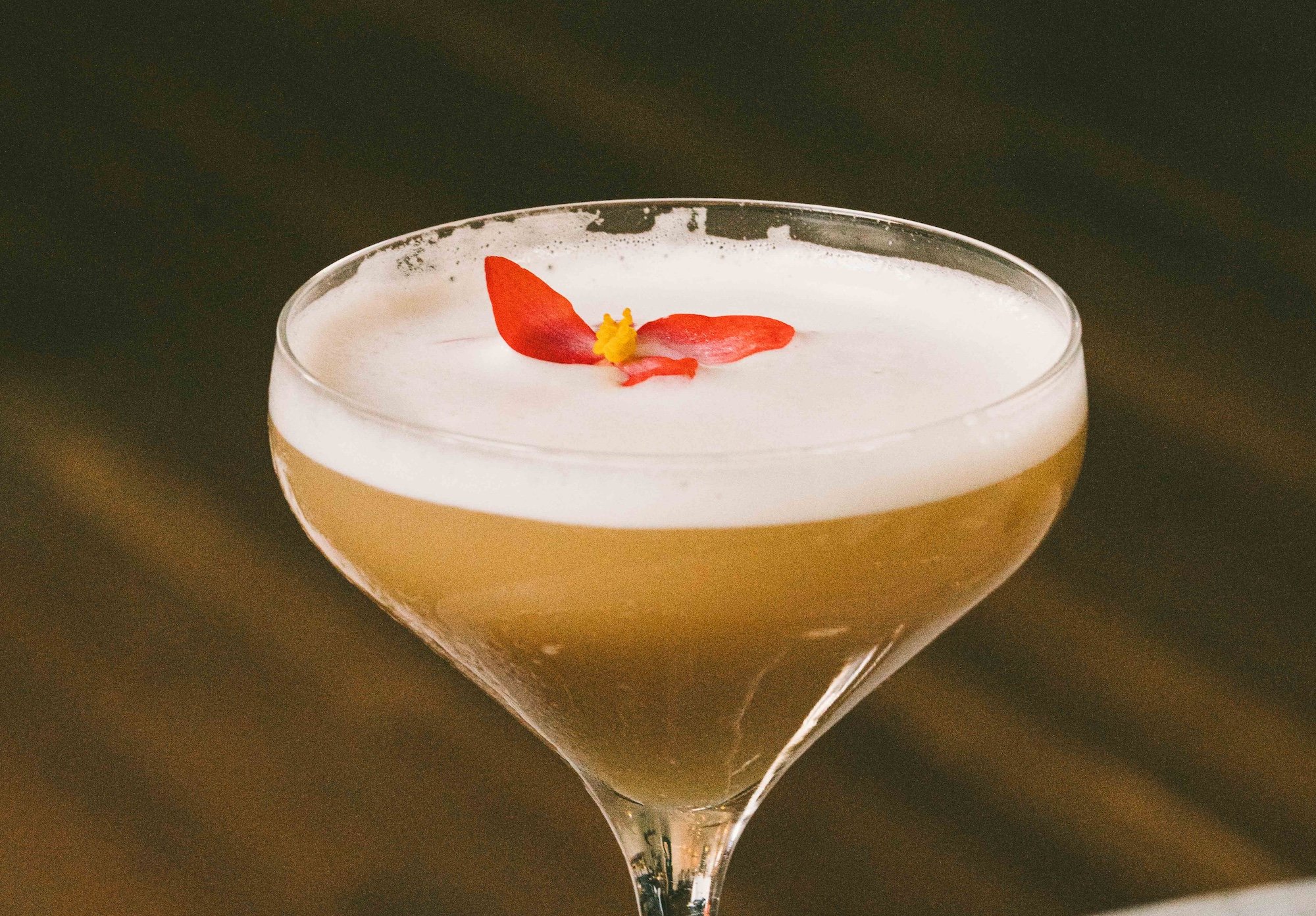 Cocktail with an egg white foam and a pink flower on top.