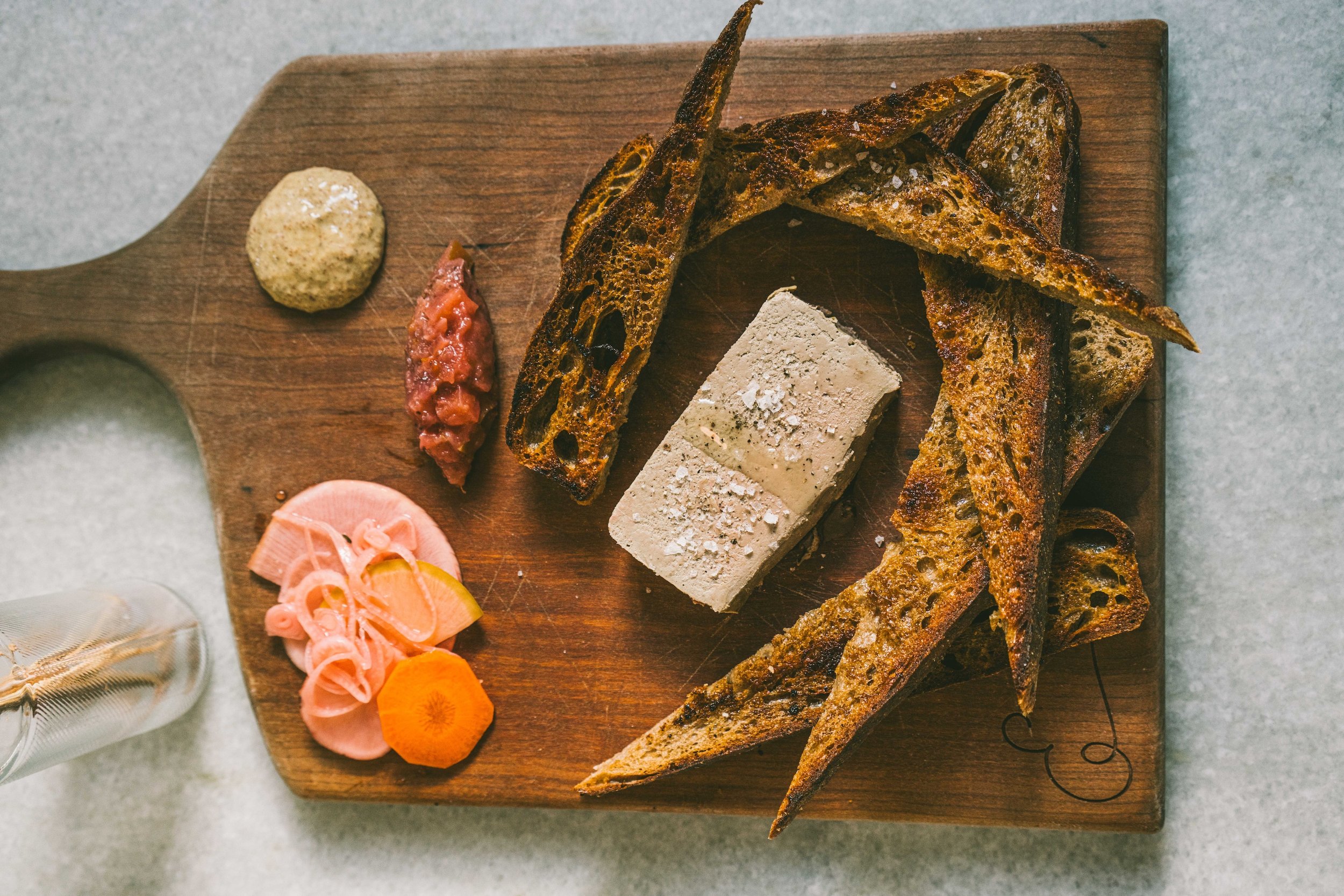 Chicken liver pate served with sourdough toast and pickled veggies on a charcuterie board.