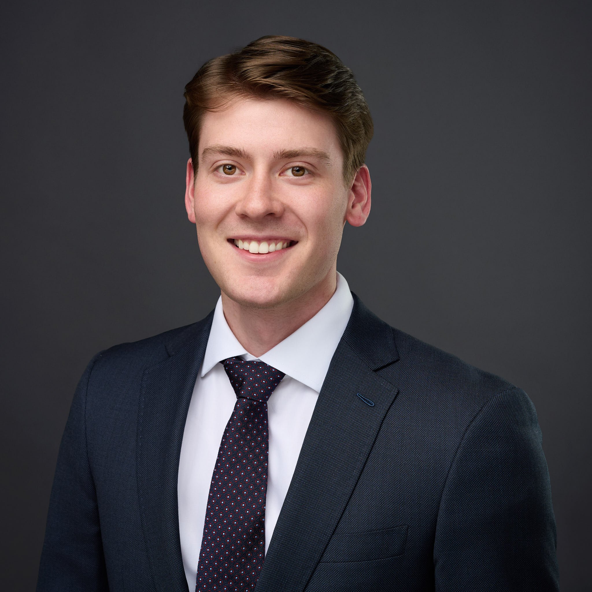 Professional headshot of a smiling man in a navy suit and patterned tie, executive studio portraiture in Westport, CT by N. Lalor Photography.