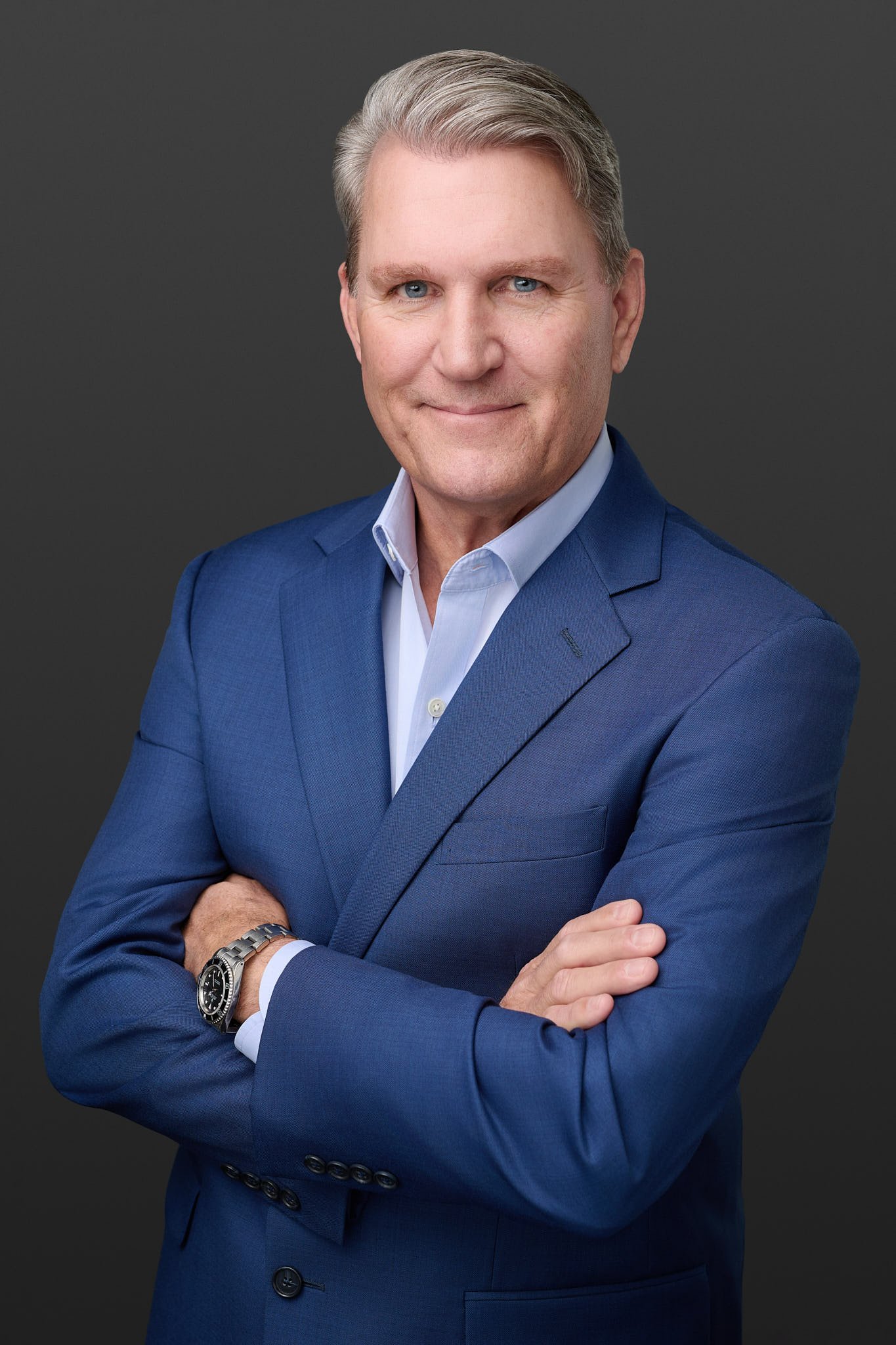 Executive business portrait of a man in a blue suit against a dark grey background, professional studio photography by N. Lalor Photography.