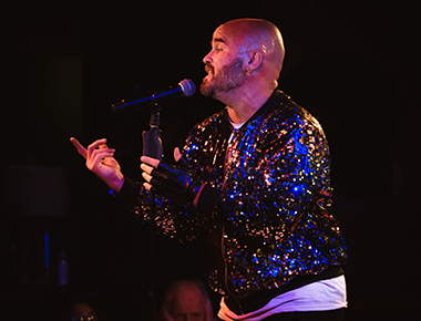Todd Alsup shines in a beautiful jacket, while singing into a microphone on stage.