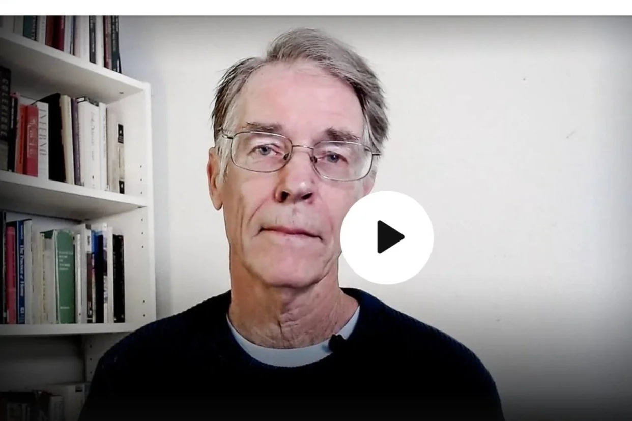 Dr. Peter Levine, Inquiring Minds advisor looking at the camera, sitting in front of a white wall and a bookshelf filled with books.