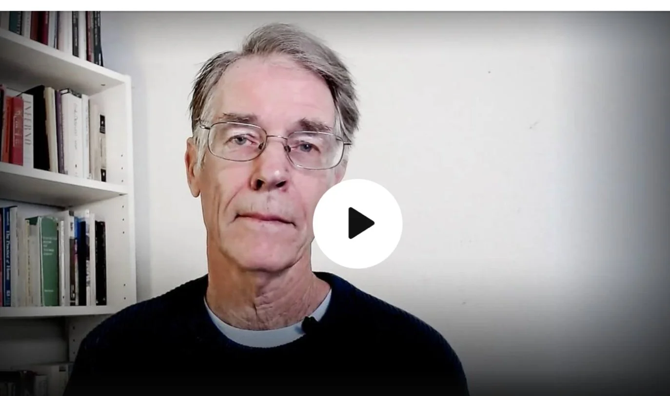 Dr. Peter Levine, Inquiring Minds' advisor in front of a white wall and bookshelves.