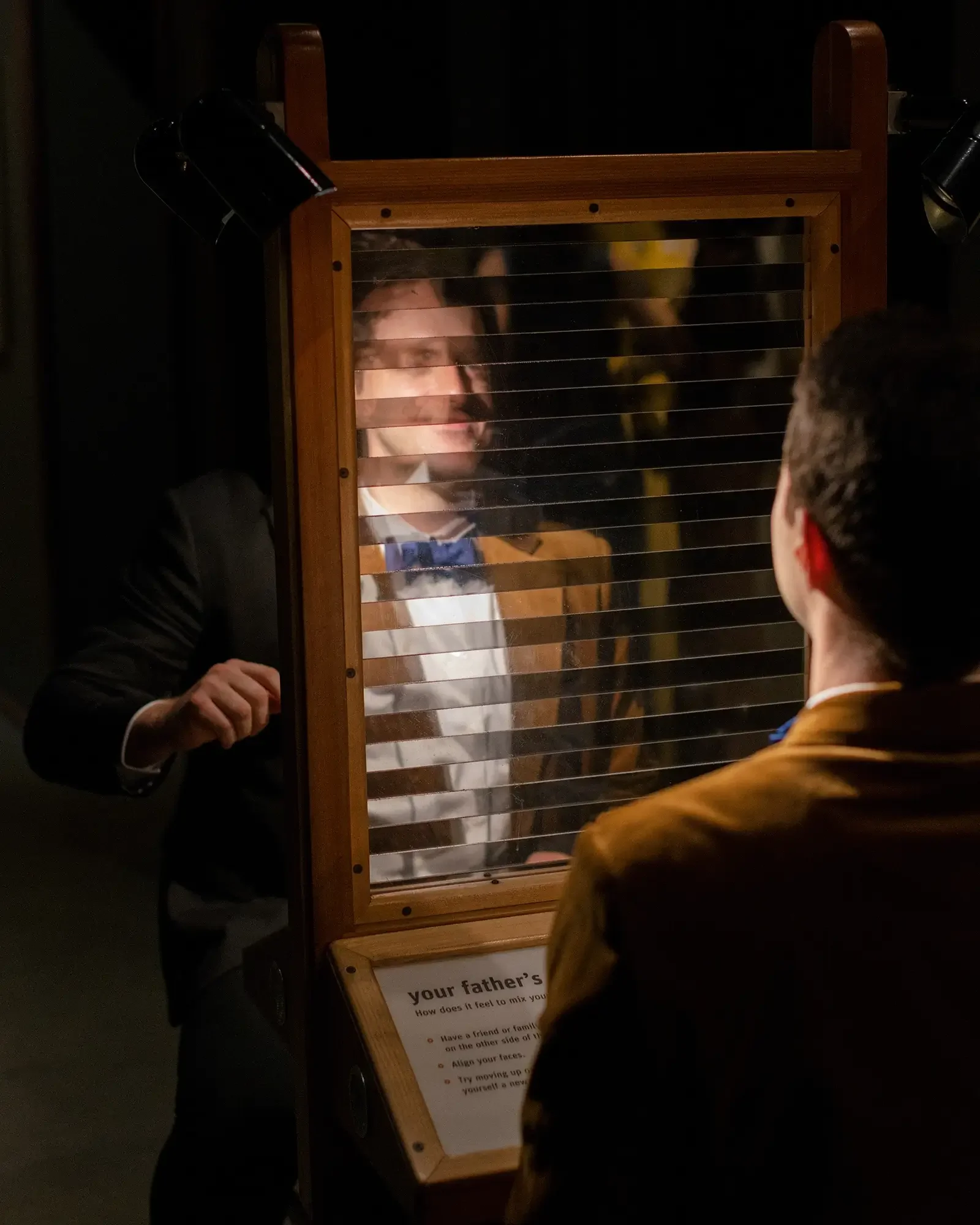 Two men playing a father-son mirror game in a dark room, with a sign explaining the activity.